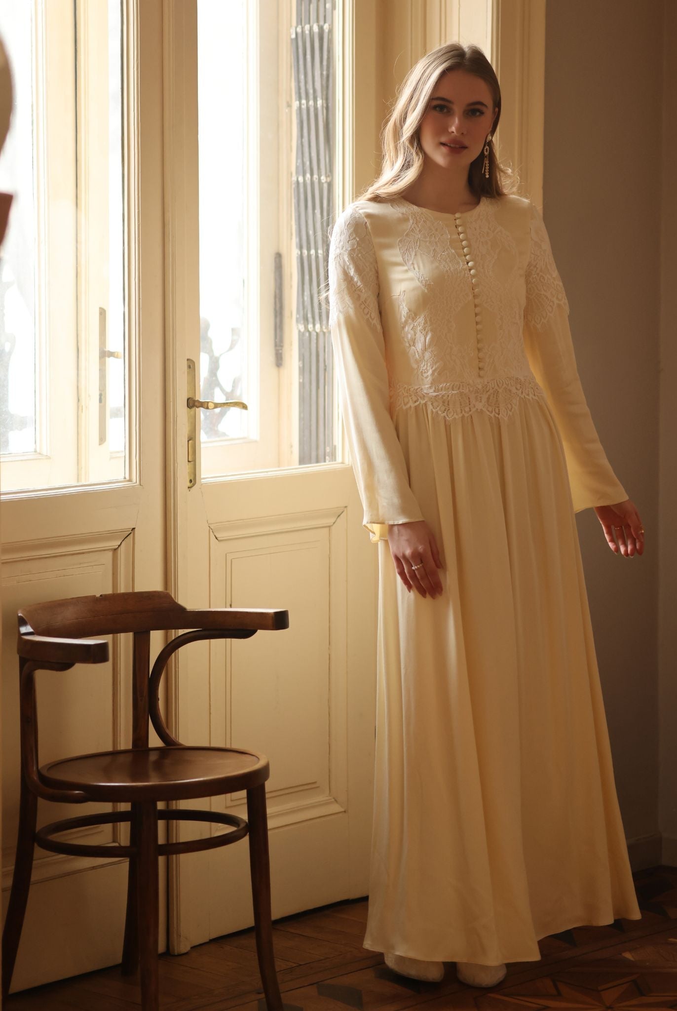 A shot by the window featuring the modest long-sleeved nightdress with a high neckline and floral lace patterns.