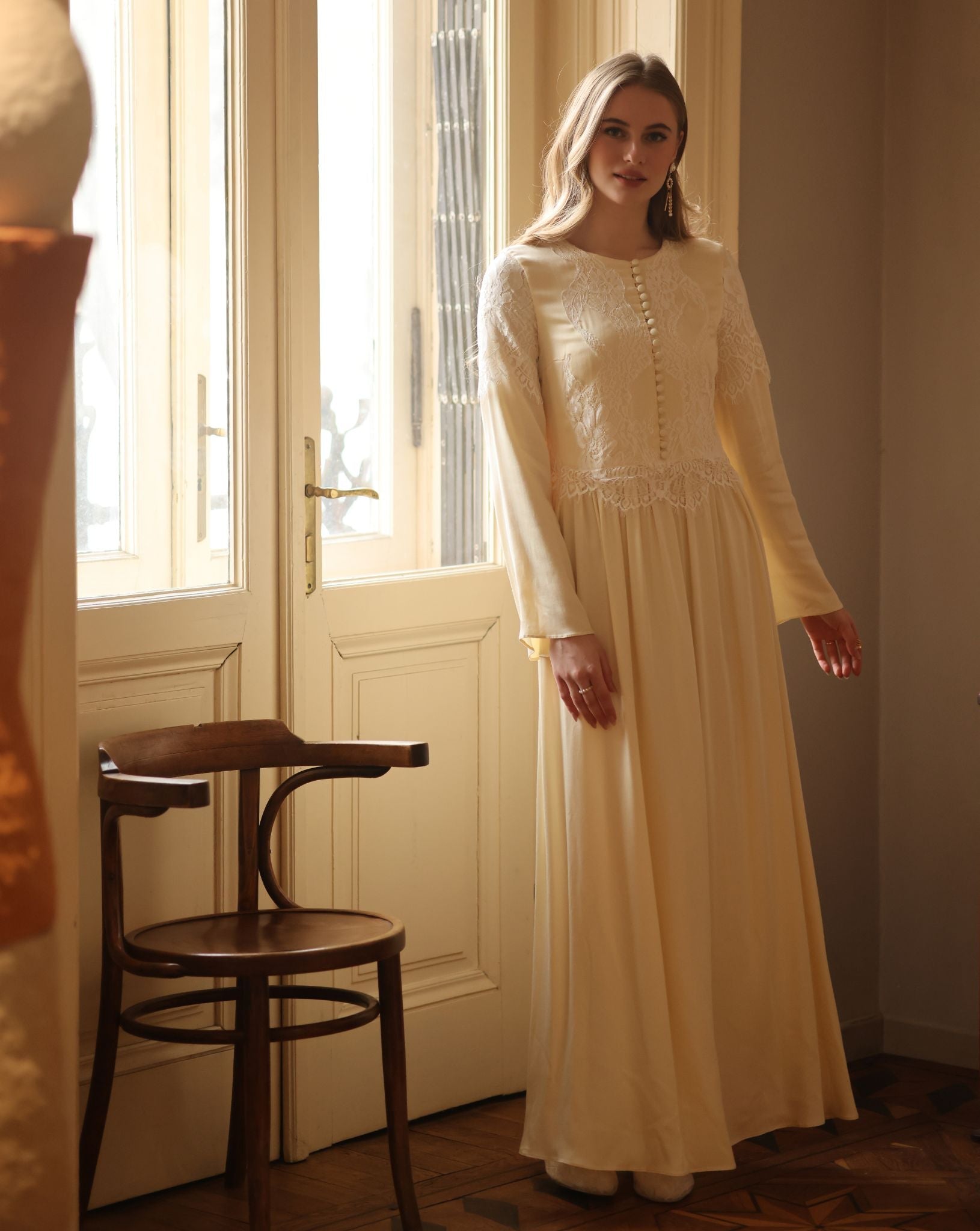 A shot by the window featuring the modest long-sleeved nightdress with a high neckline and floral lace patterns.