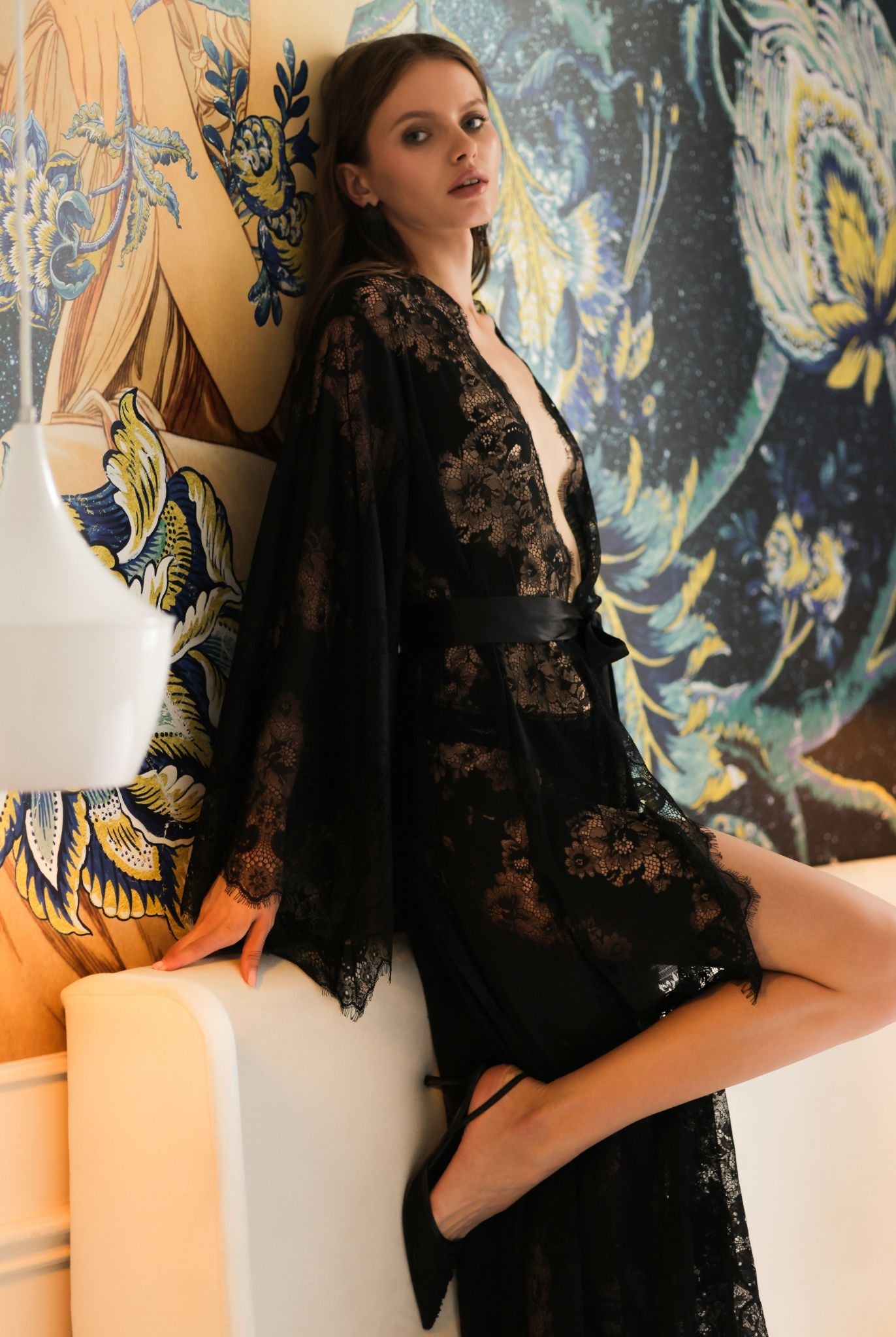 Graceful pose on a bed in a sheer black lace garment, emphasizing a romantic and sophisticated evening look.