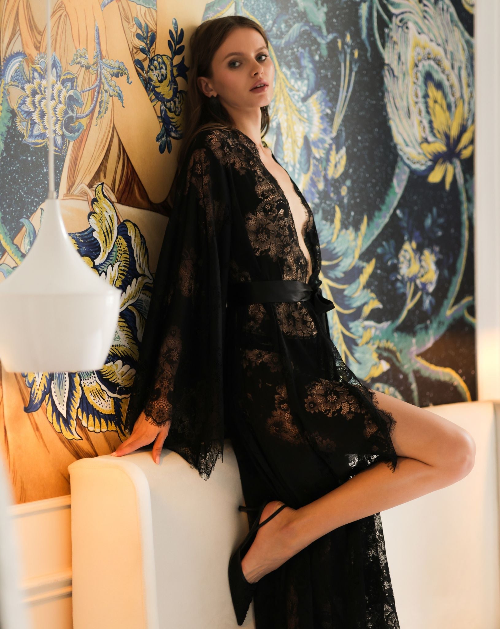 Graceful pose on a bed in a sheer black lace garment, emphasizing a romantic and sophisticated evening look.