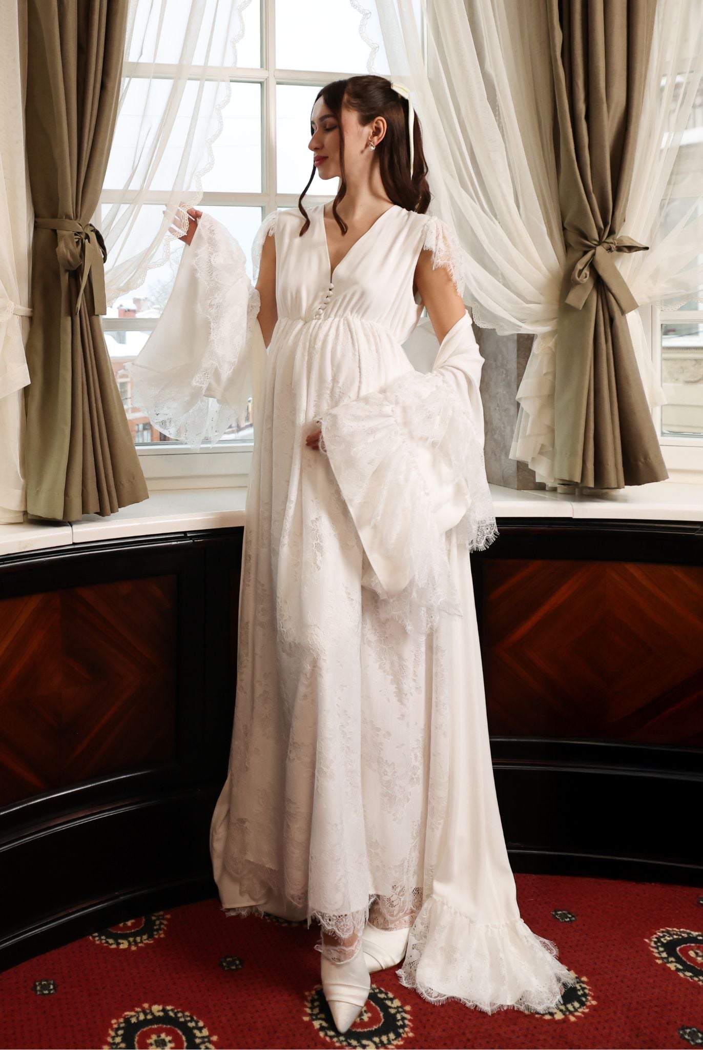 A creative shot of an expecting woman by the window, with the robe draped gently over the shoulders.