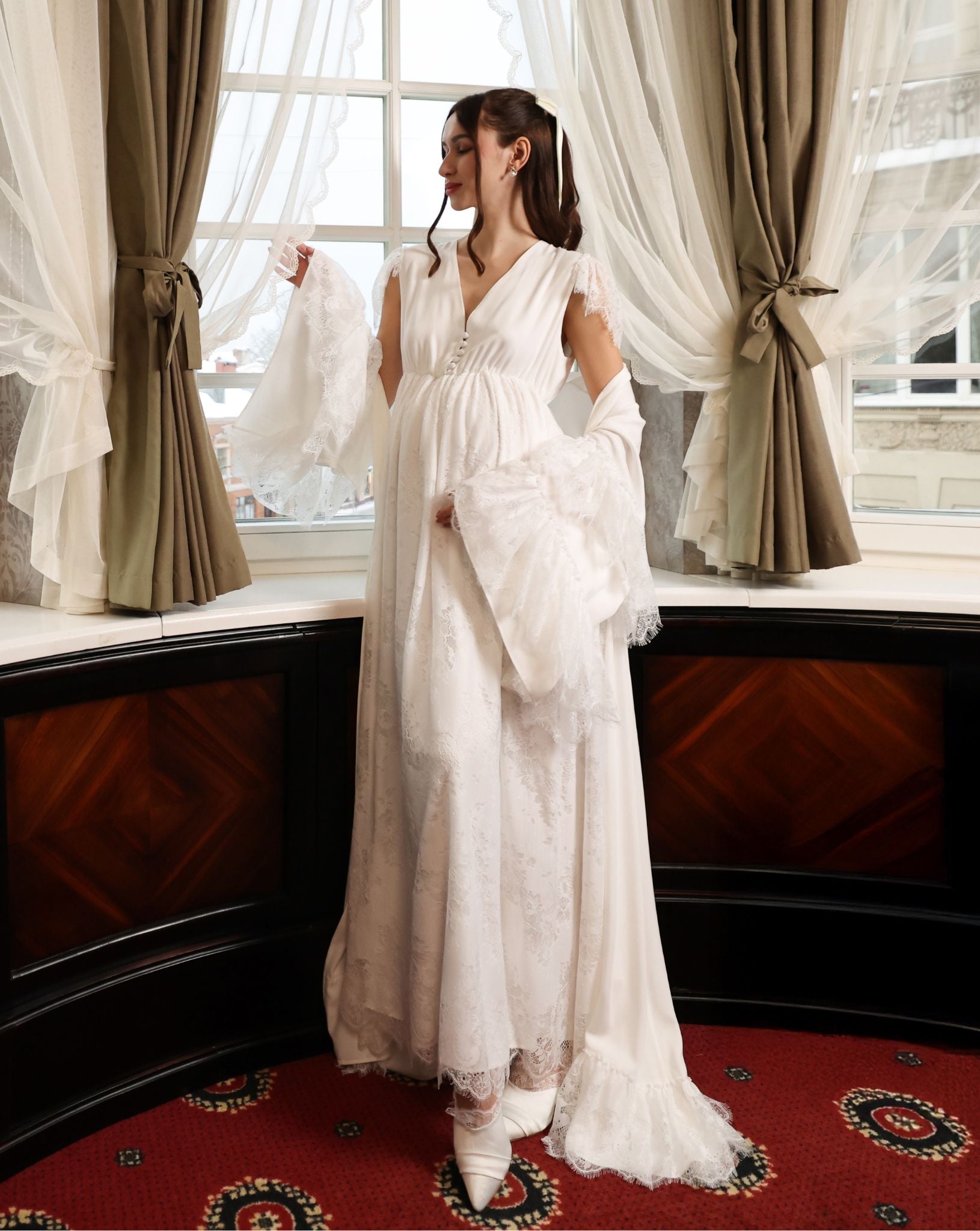 A creative shot of an expecting woman by the window, with the robe draped gently over the shoulders.