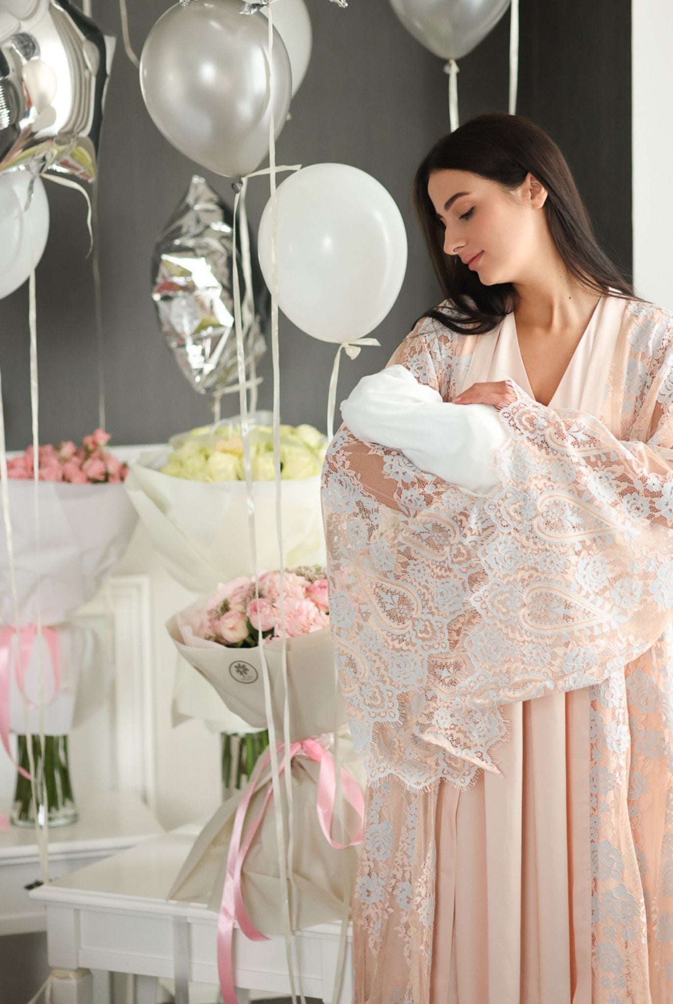A woman holding a newborn while wearing a delicate lace Maternity Robe and Nightgown Set in a soft home setting.