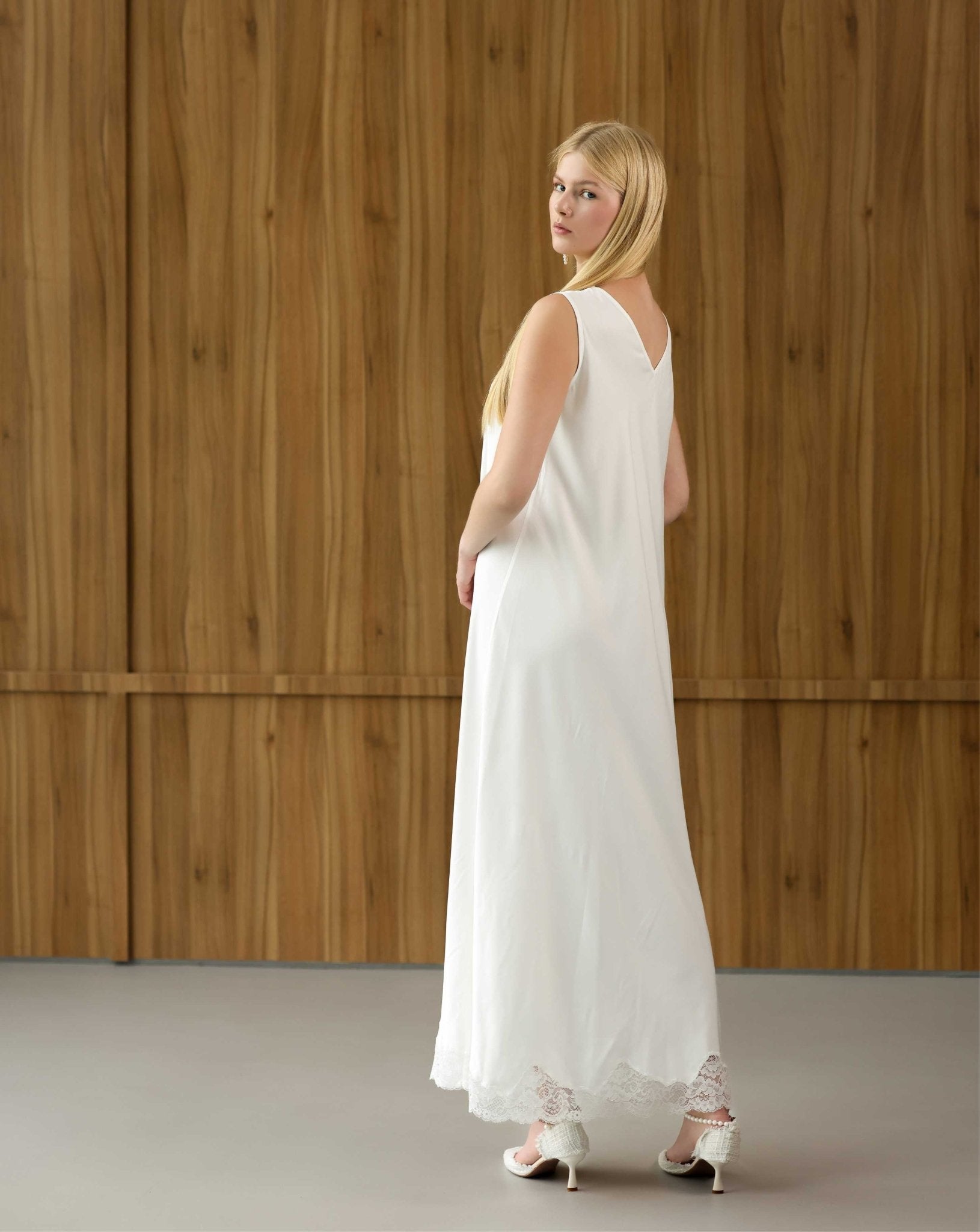Side view of the white maternity nightgown, showcasing the open V-cut back and delicate lace-trimmed hem.