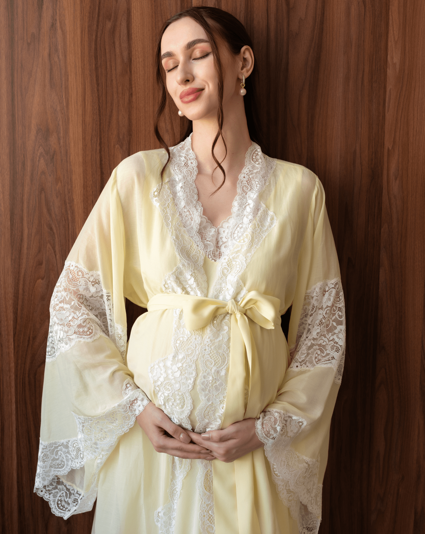 Tender maternity shot in a yellow cotton robe with a sash tied over the baby bump, highlighting soft lace details.