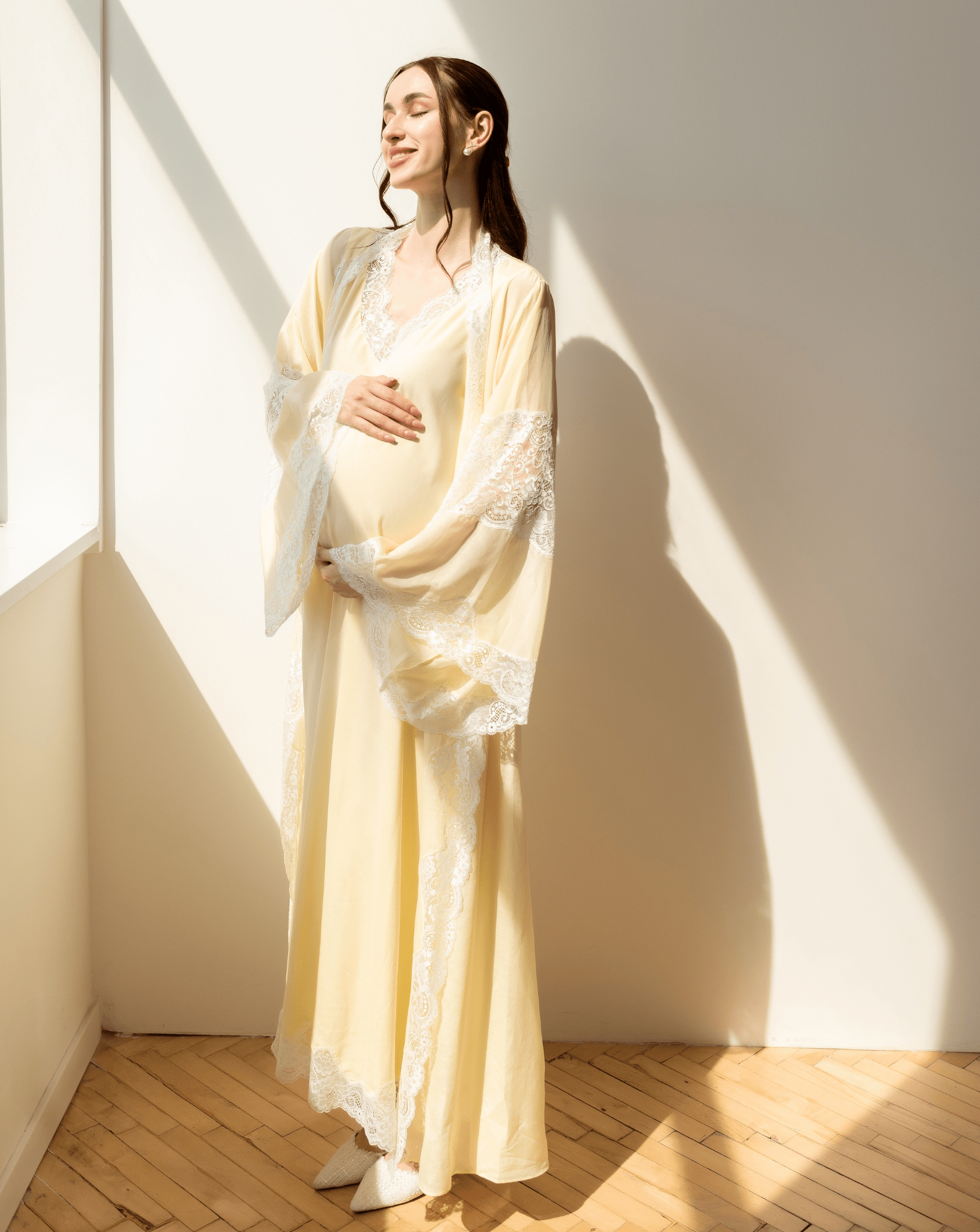 Serene portrait in sunlight, holding a baby bump in a long yellow gown for a tender and graceful maternity look.