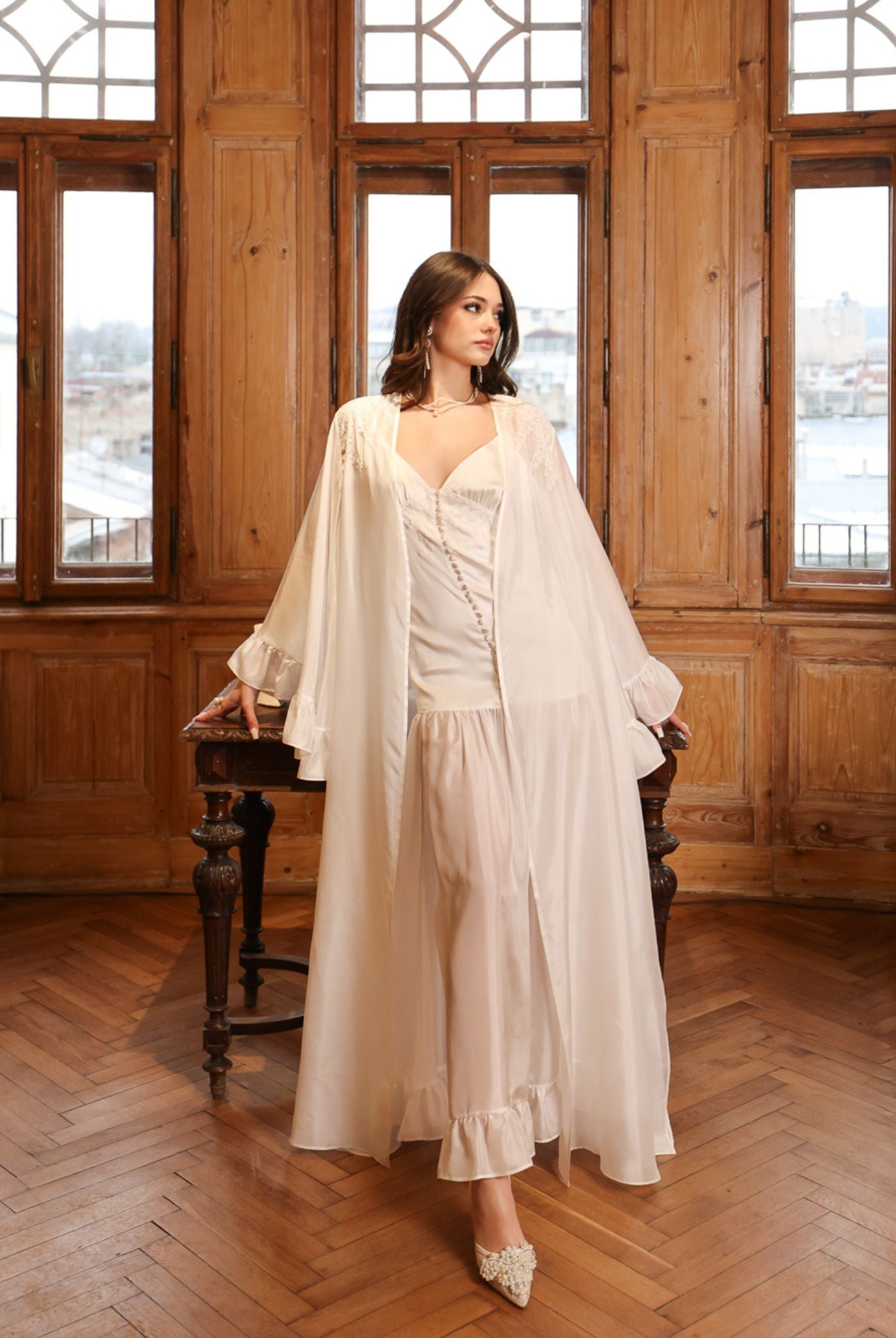 Sophisticated pose leaning on a table, showcasing the luxurious drape of the long silk robe and satin inner dress.
