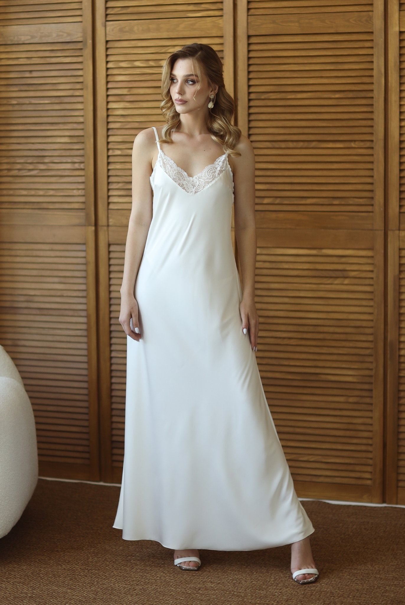 Bride in flowing white robe and nightgown, standing near wood panel