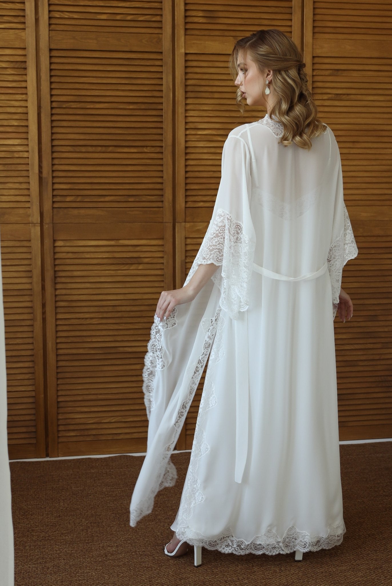 Bride adjusting lace robe sleeves in bridal suite