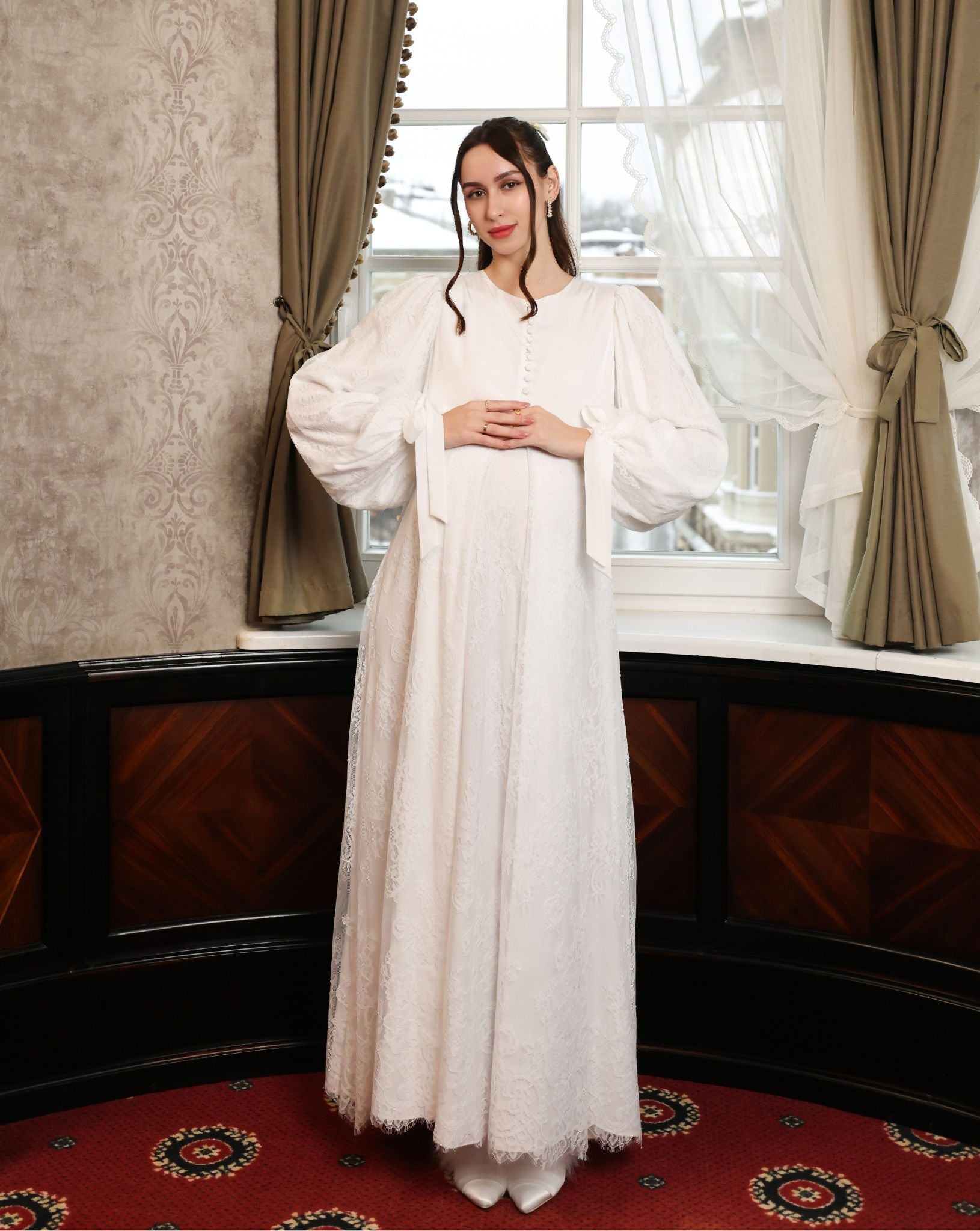 Frontal shot of an expecting woman with hands on the waist, highlighting the delicate ruffle framing the waistline.