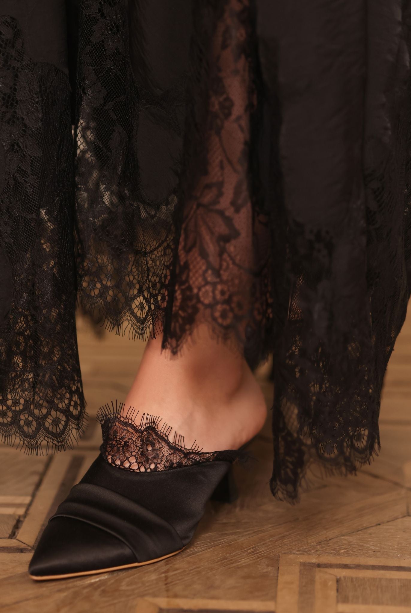 Close-up of the slipper on one foot, highlighting the delicate French lace adornment and meticulous craftsmanship.