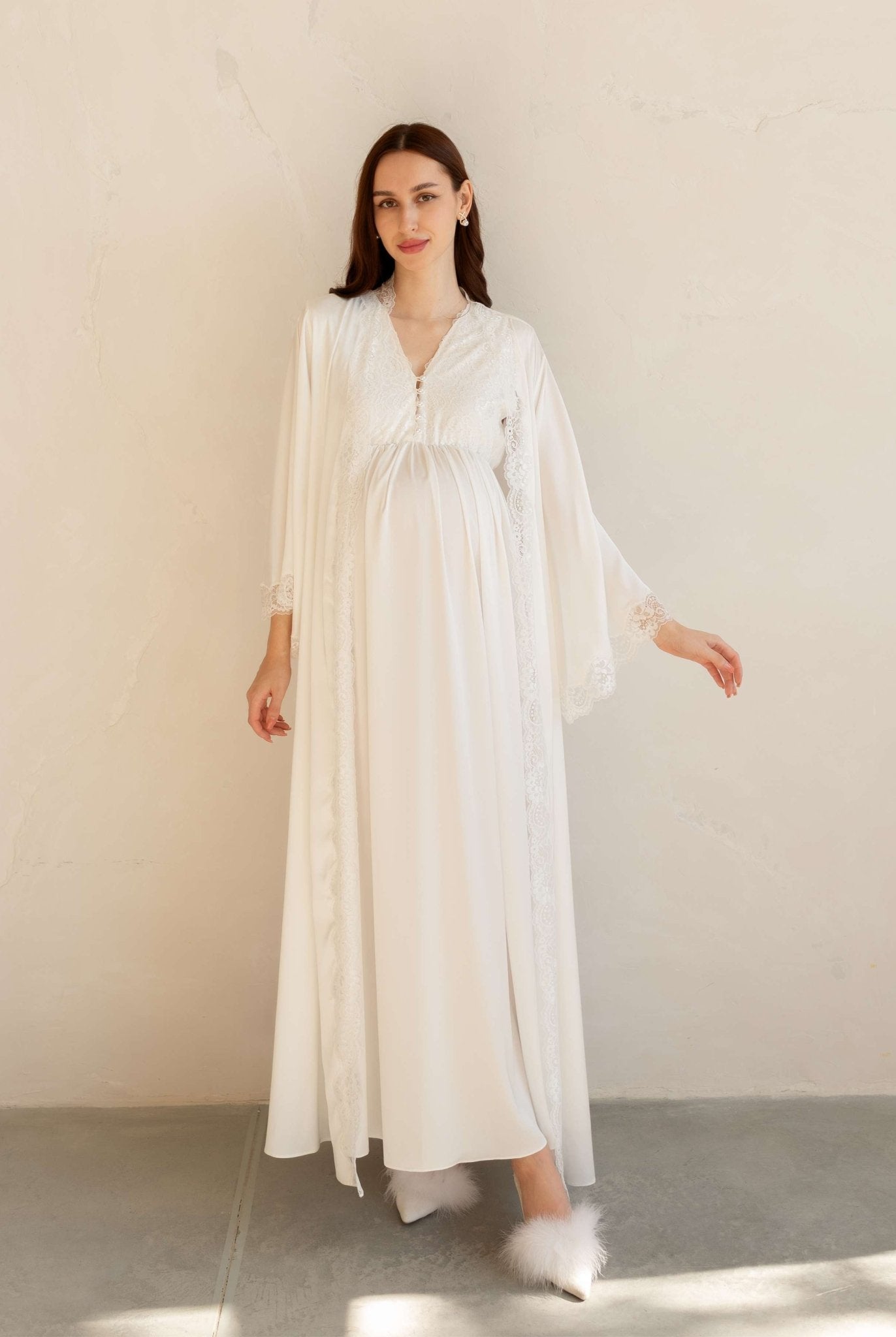 Full-length view of a white maternity robe with a belt tied over the baby bump, featuring wide lace-trimmed sleeves.