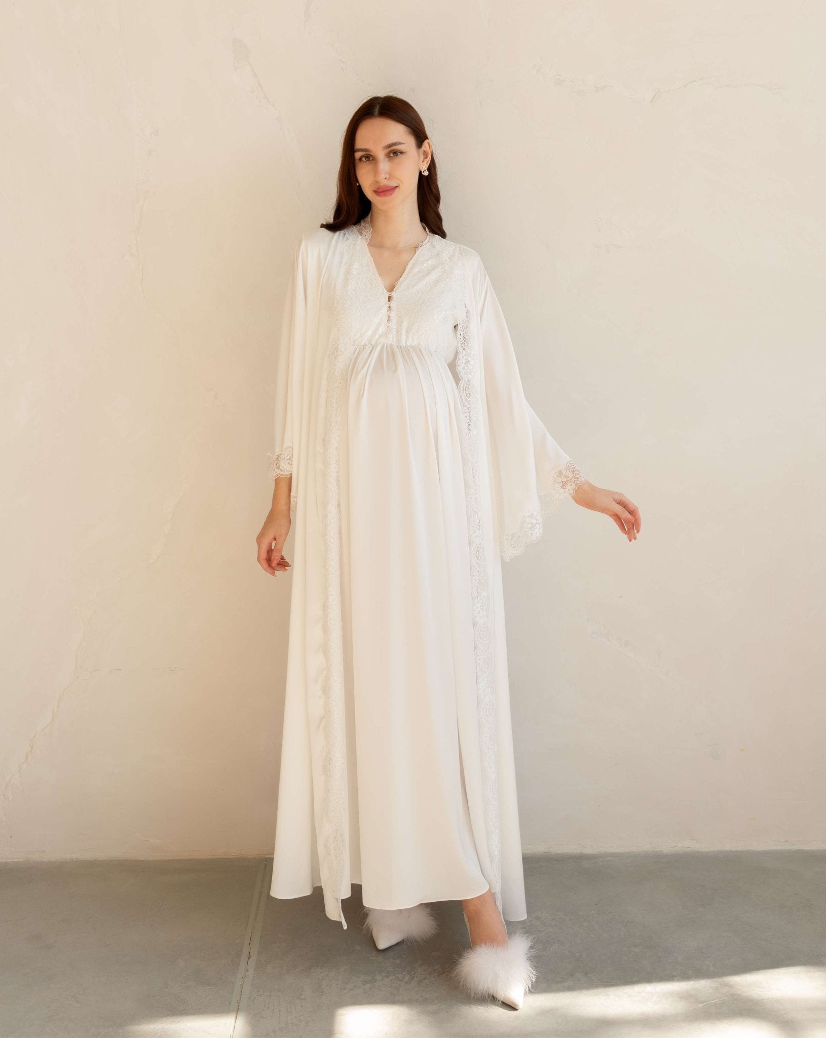 Full-length view of a white maternity robe with a belt tied over the baby bump, featuring wide lace-trimmed sleeves.