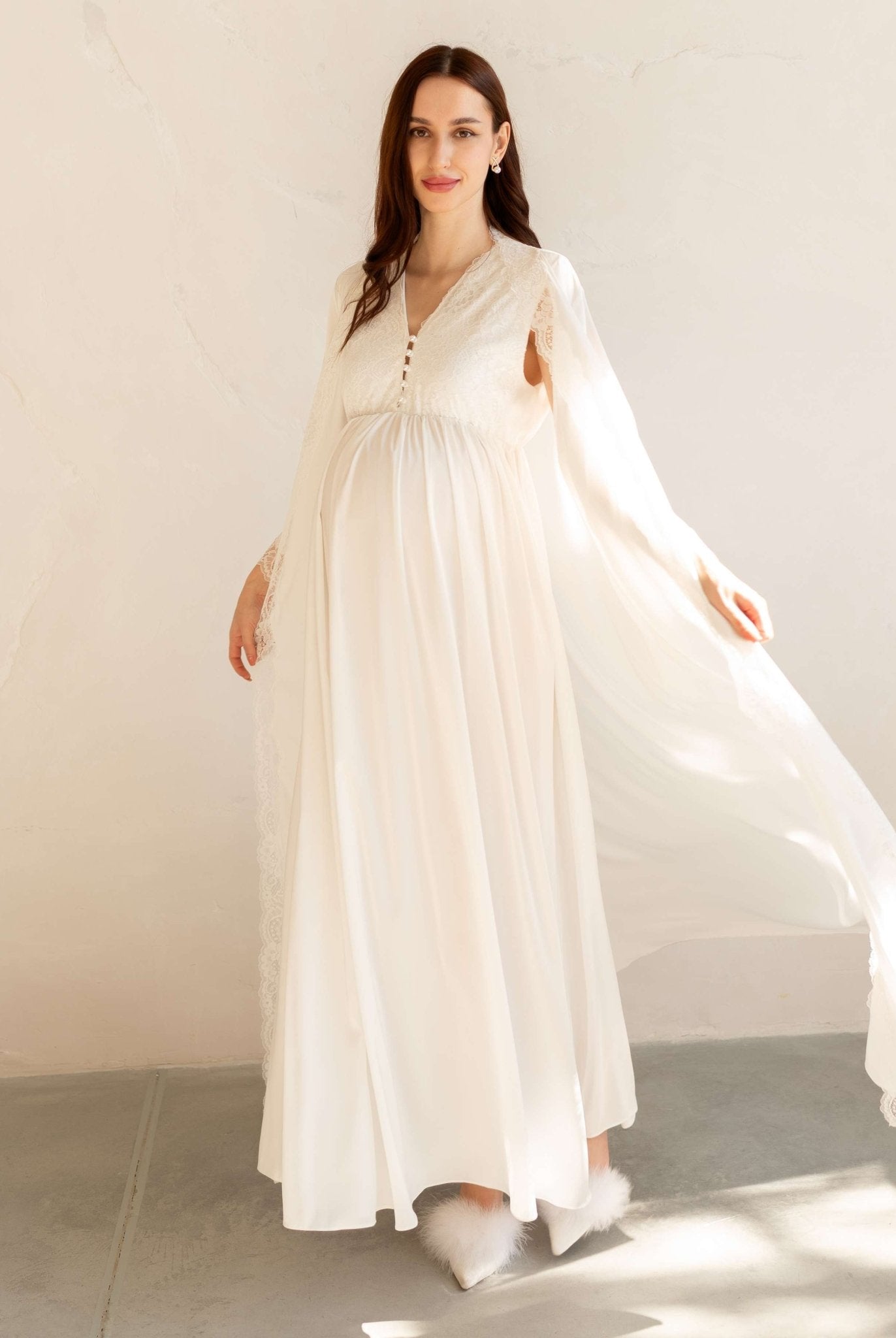 Pregnant woman in a white lace robe that flows beautifully in the air, highlighting a graceful silhouette.