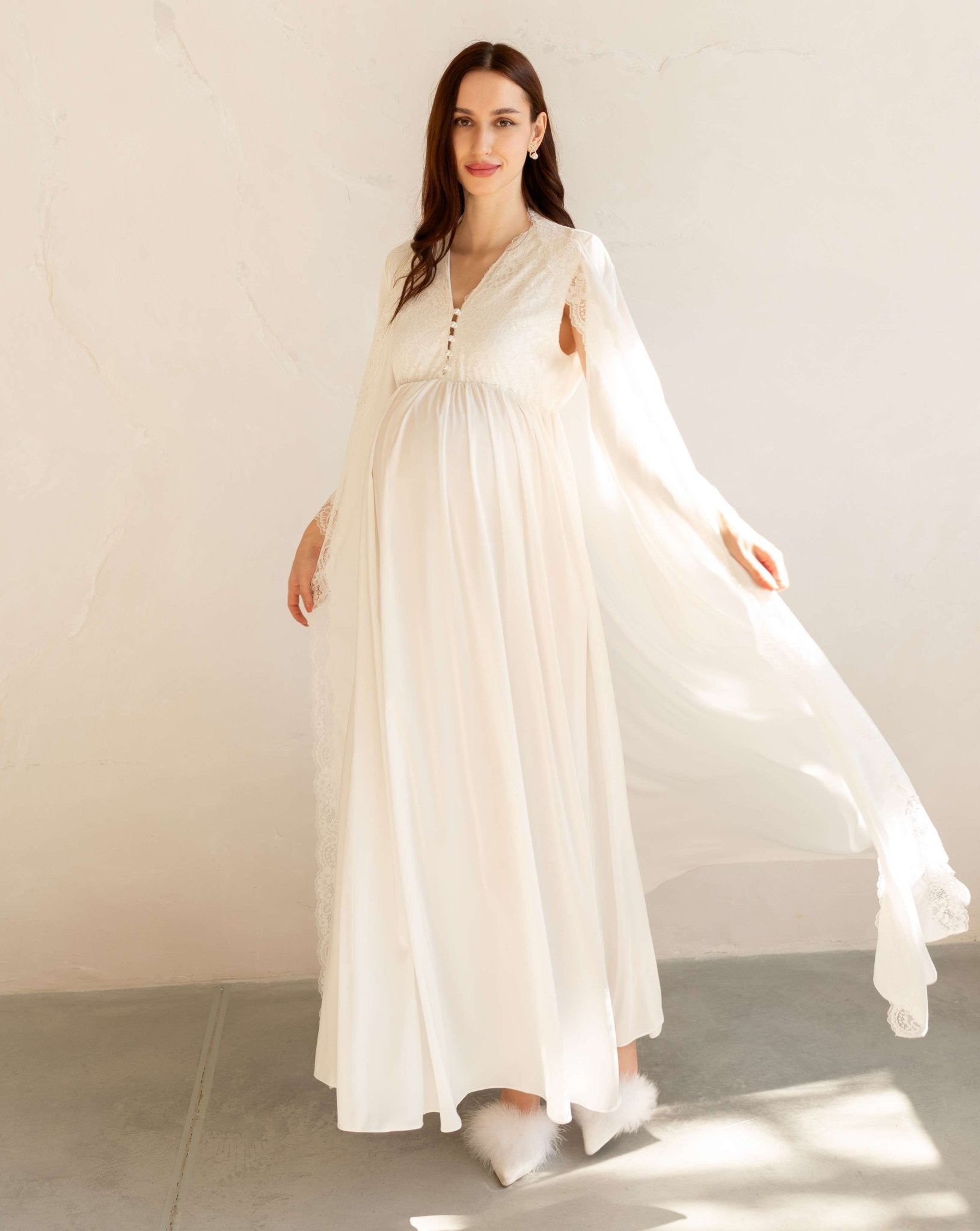 Pregnant woman in a white lace robe that flows beautifully in the air, highlighting a graceful silhouette.