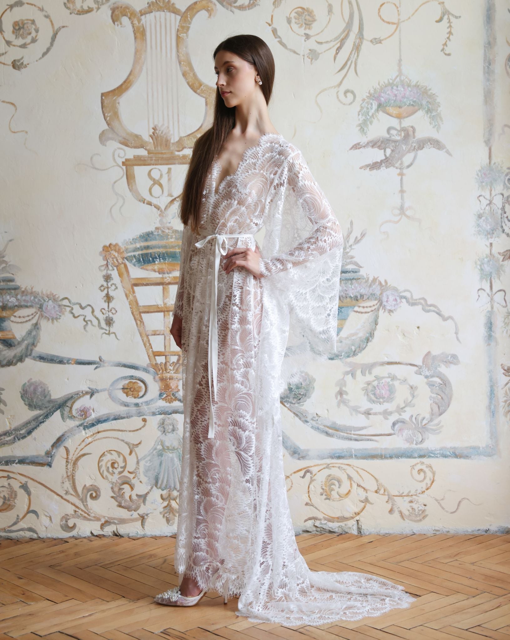Side profile of the lace bridal garment, highlighting the dramatic floor-length train and defined silhouette.