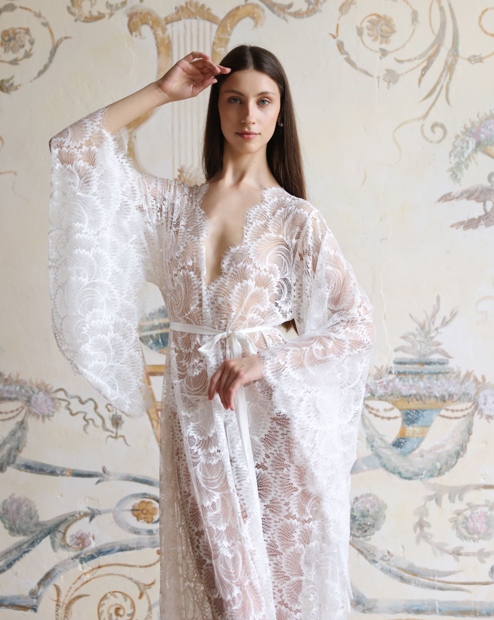 Mid-length shot of a white lace garment with a hand raised, highlighting the wide, airy sleeves and intricate patterns.