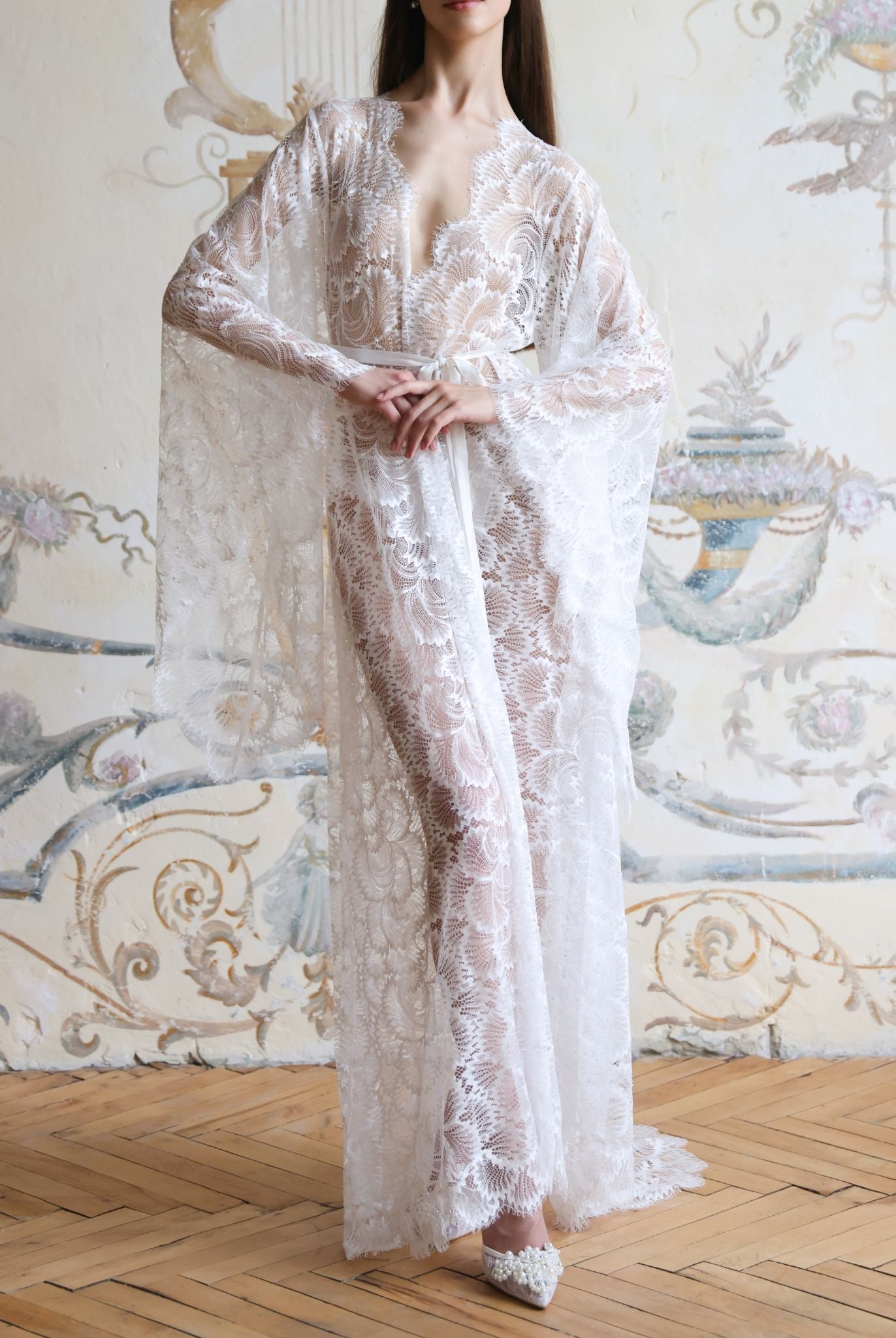 Elegant full-length shot of a white sheer lace robe with a hand on the waist, showcasing the flowing hem and train.