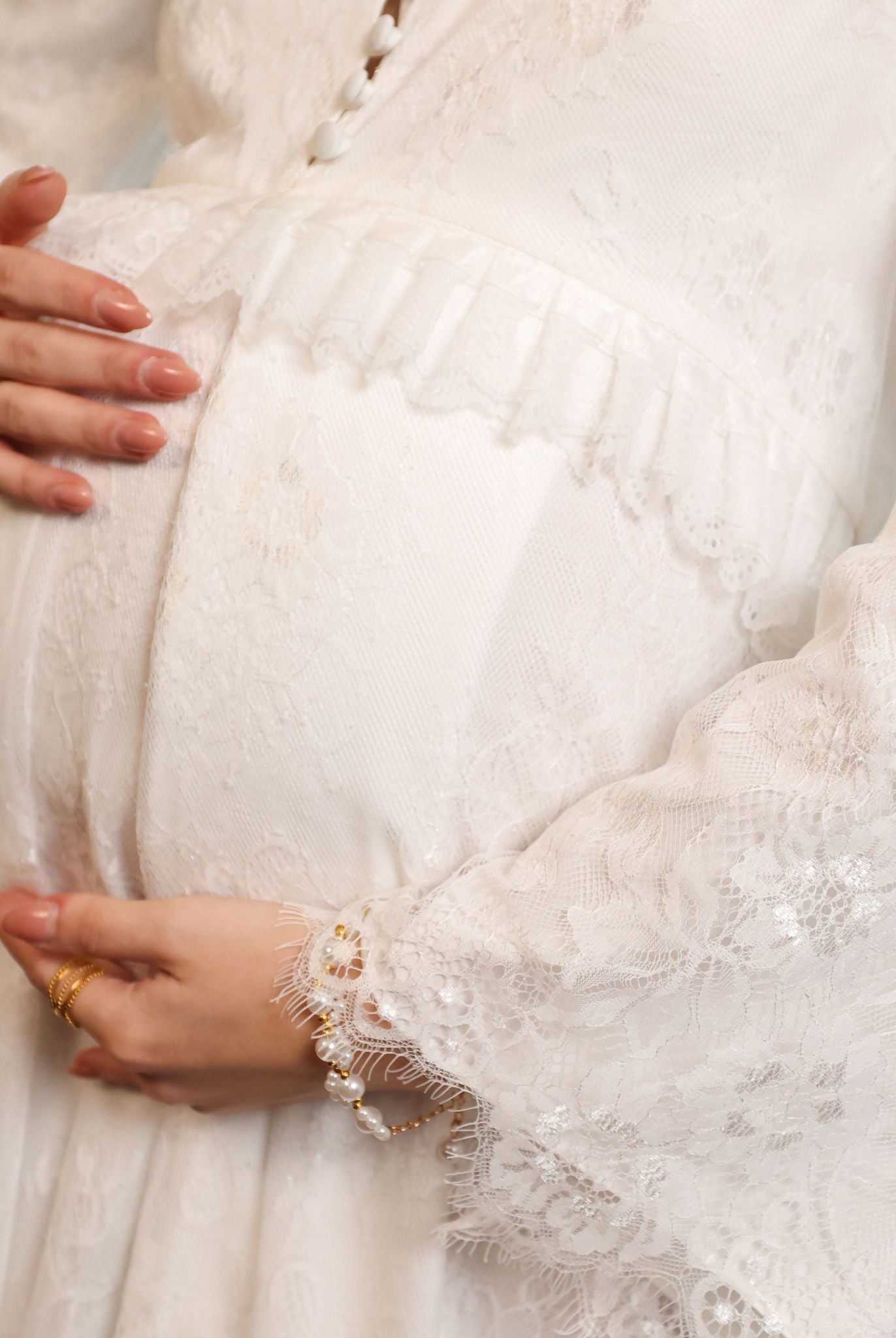 Close-up maternity shot focusing on the lace-embellished sleeves and the delicate ruffle framing the waistline.