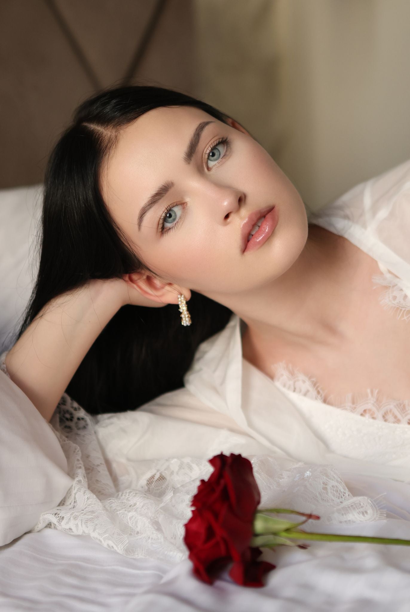 Creative shot of a woman lying on a bed with a red rose, wearing a soft lace-trimmed silk-cotton garment.