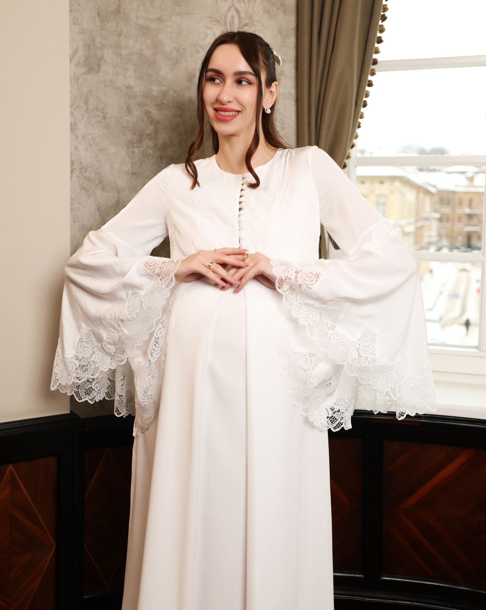 Mid-length shot of an expecting woman featuring wide sleeves with fine lace accents and a buttoned front.