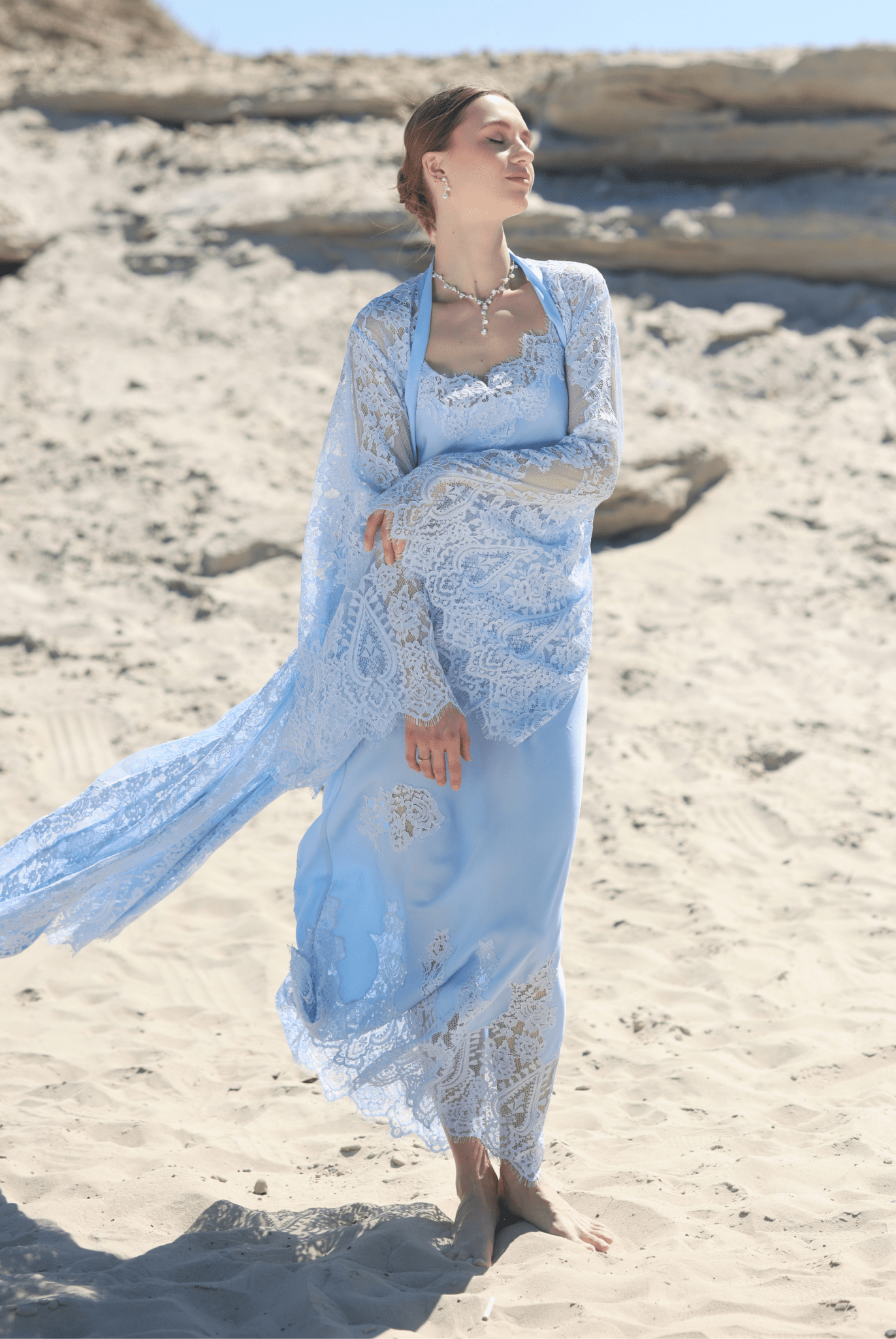 A dynamic shot of the Robe and Nightgown Set on the sand, capturing the artistic lace appliqués and flowing silhouette.