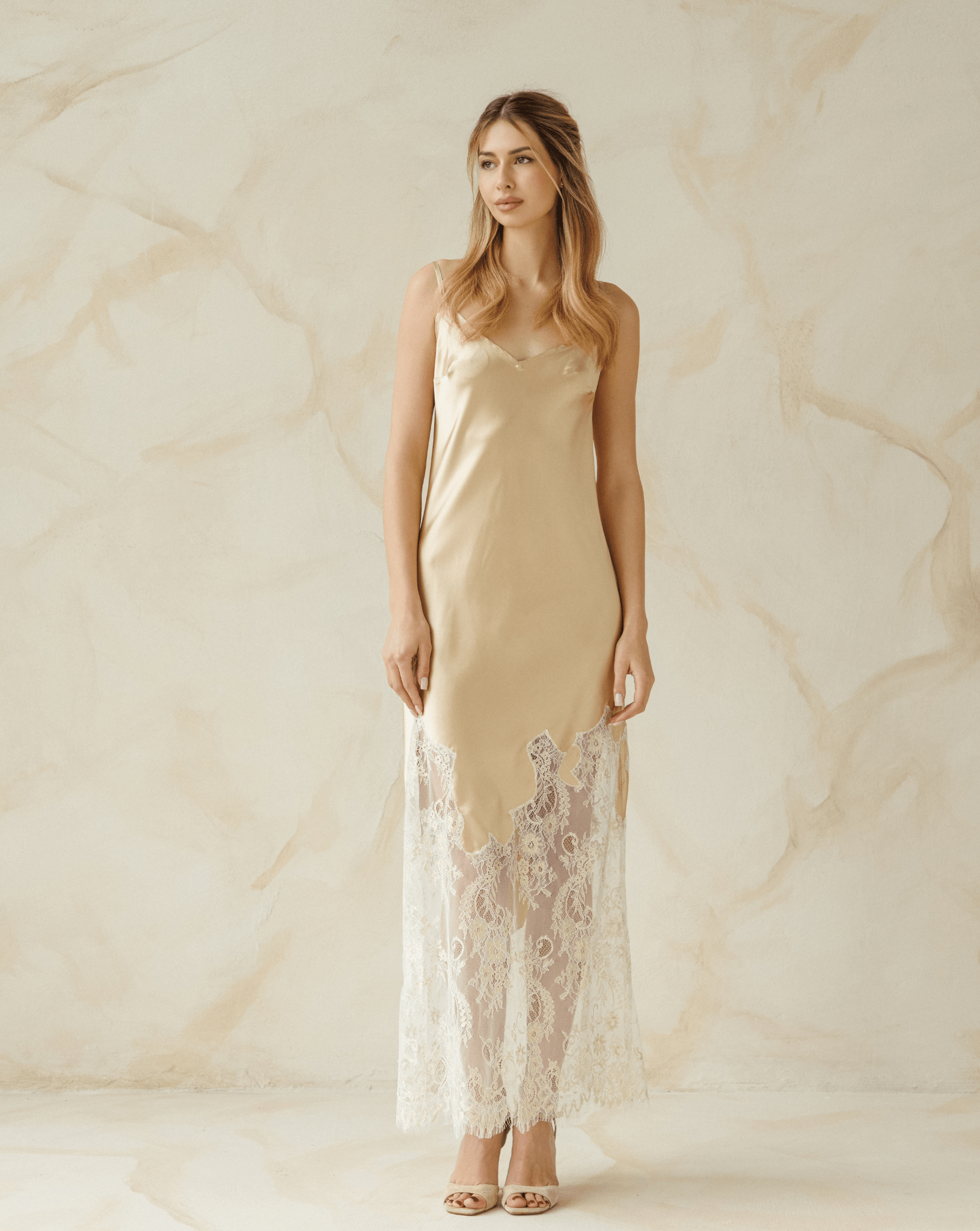 Model in beige satin nightgown with lace hem, standing in natural light