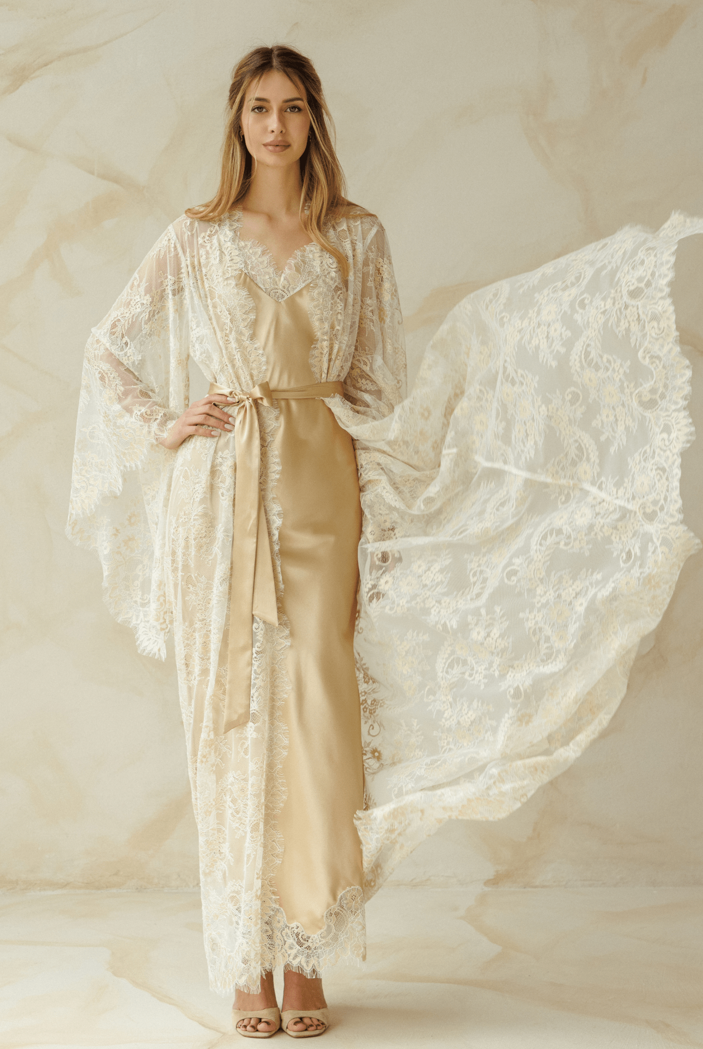 Model posing in an ivory lace robe over a long nightdress, arms slightly lifted