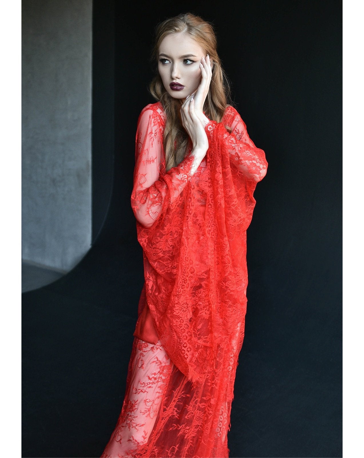 Woman in red lace robe standing against dark backdrop