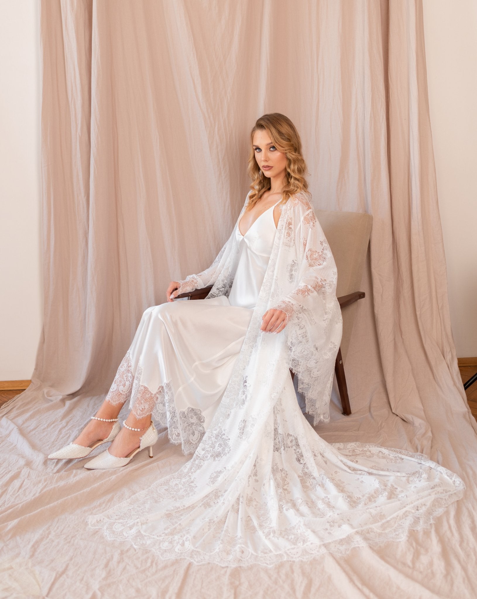 Woman sitting on floor wearing long white lace robe and nightgown, soft curtain backdrop