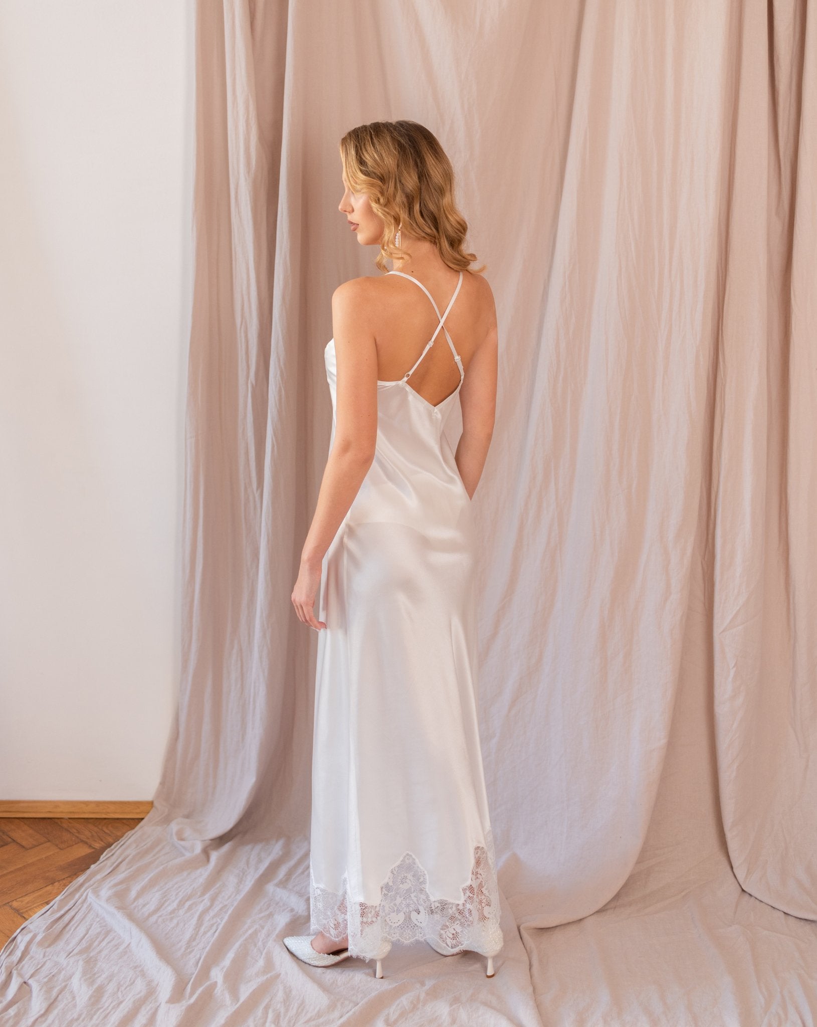 Woman in white nightgown with open back, standing in profile against soft beige backdrop