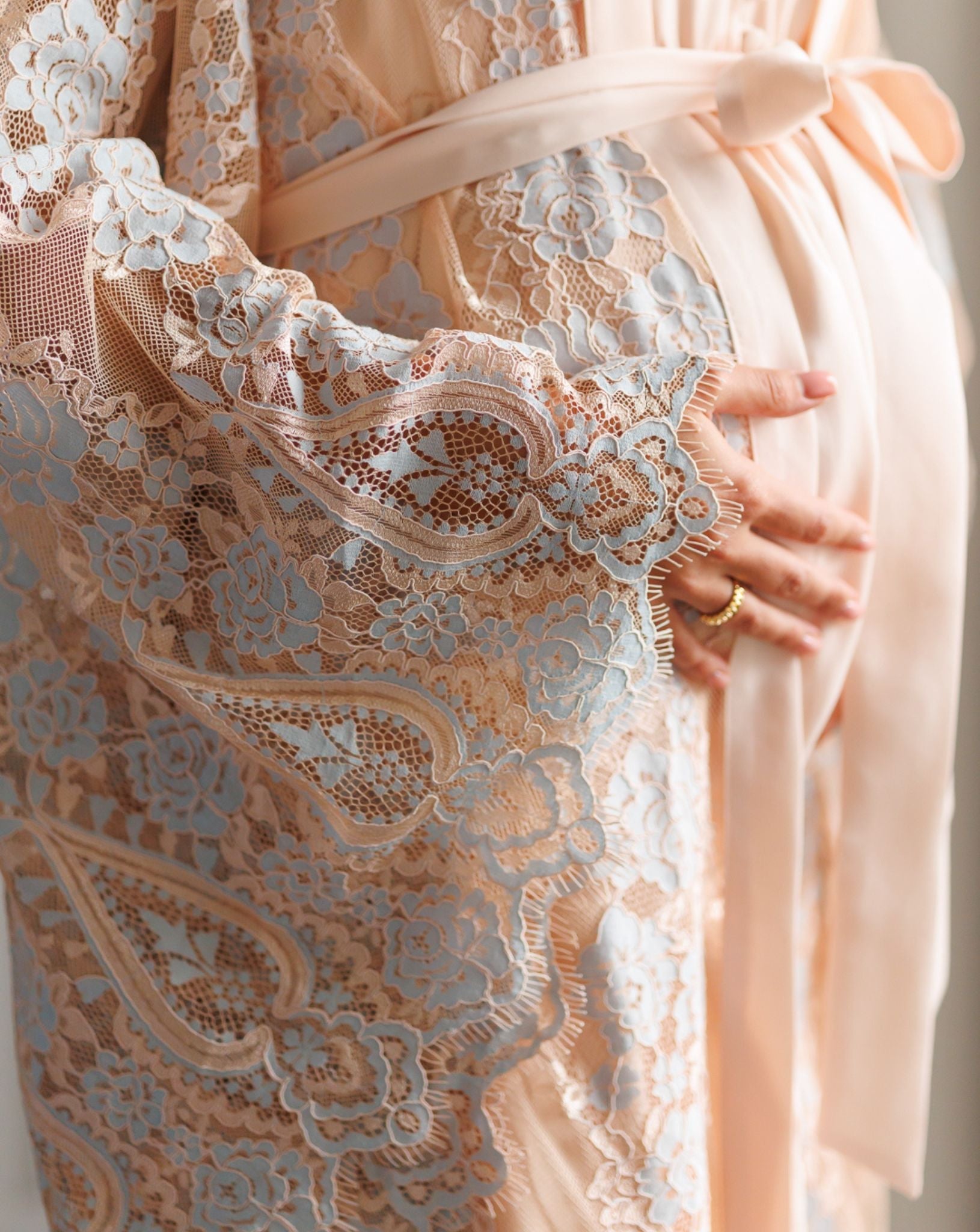 Close-up of intricate lace sleeves and hands on a pregnancy belly, capturing the feminine romance of the fabric.
