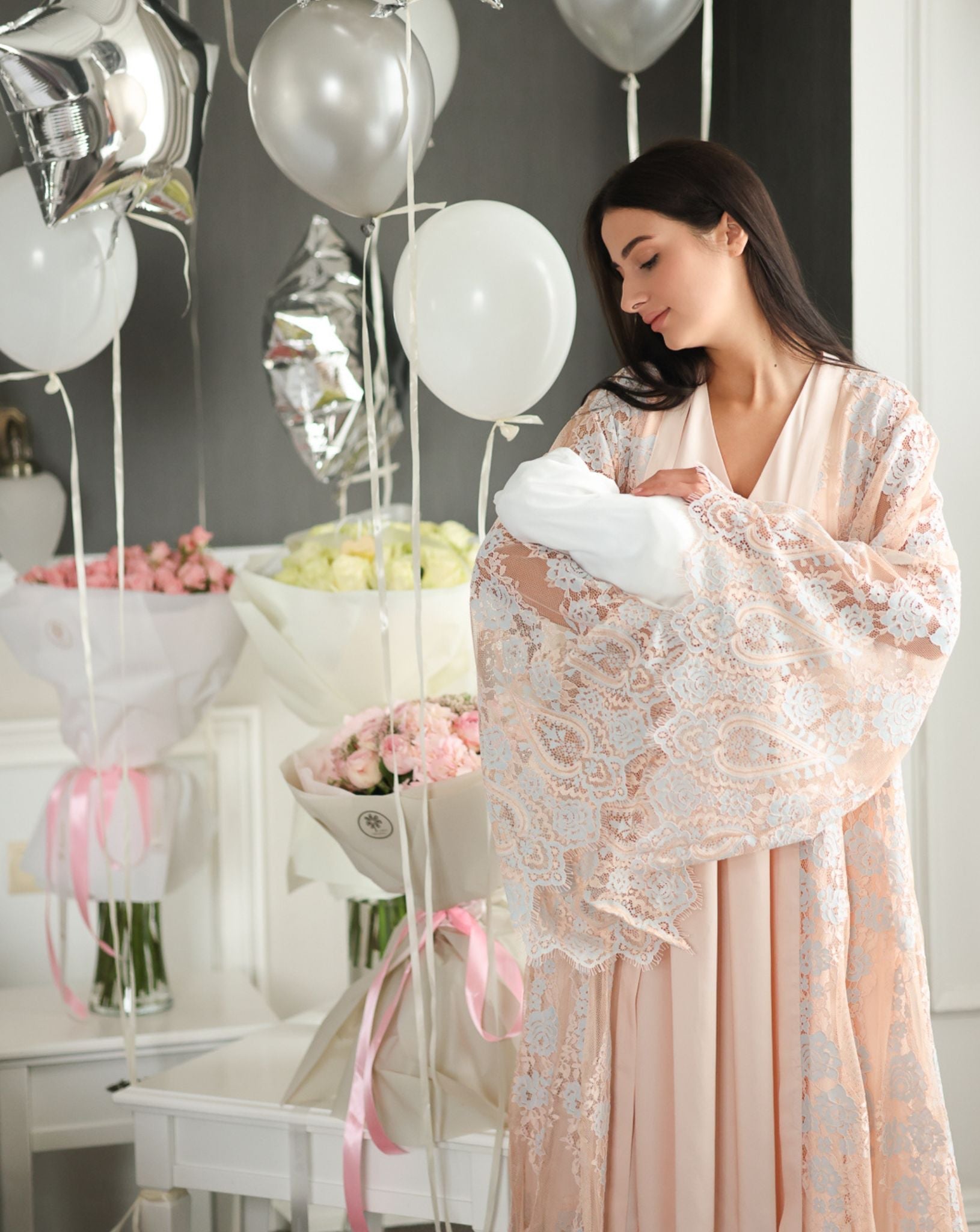 A woman holding a newborn while wearing a delicate lace Maternity Robe and Nightgown Set in a soft home setting.