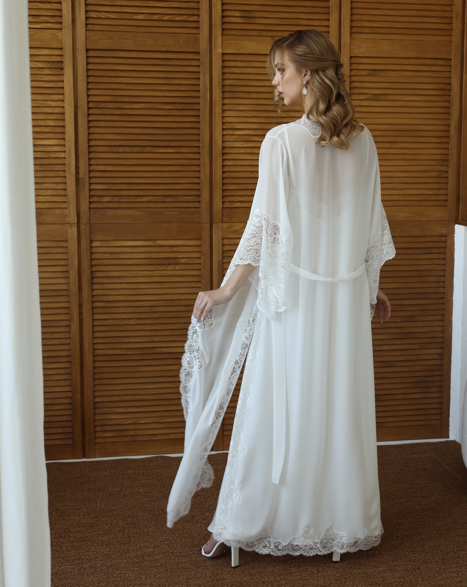 Bride adjusting lace robe sleeves in bridal suite