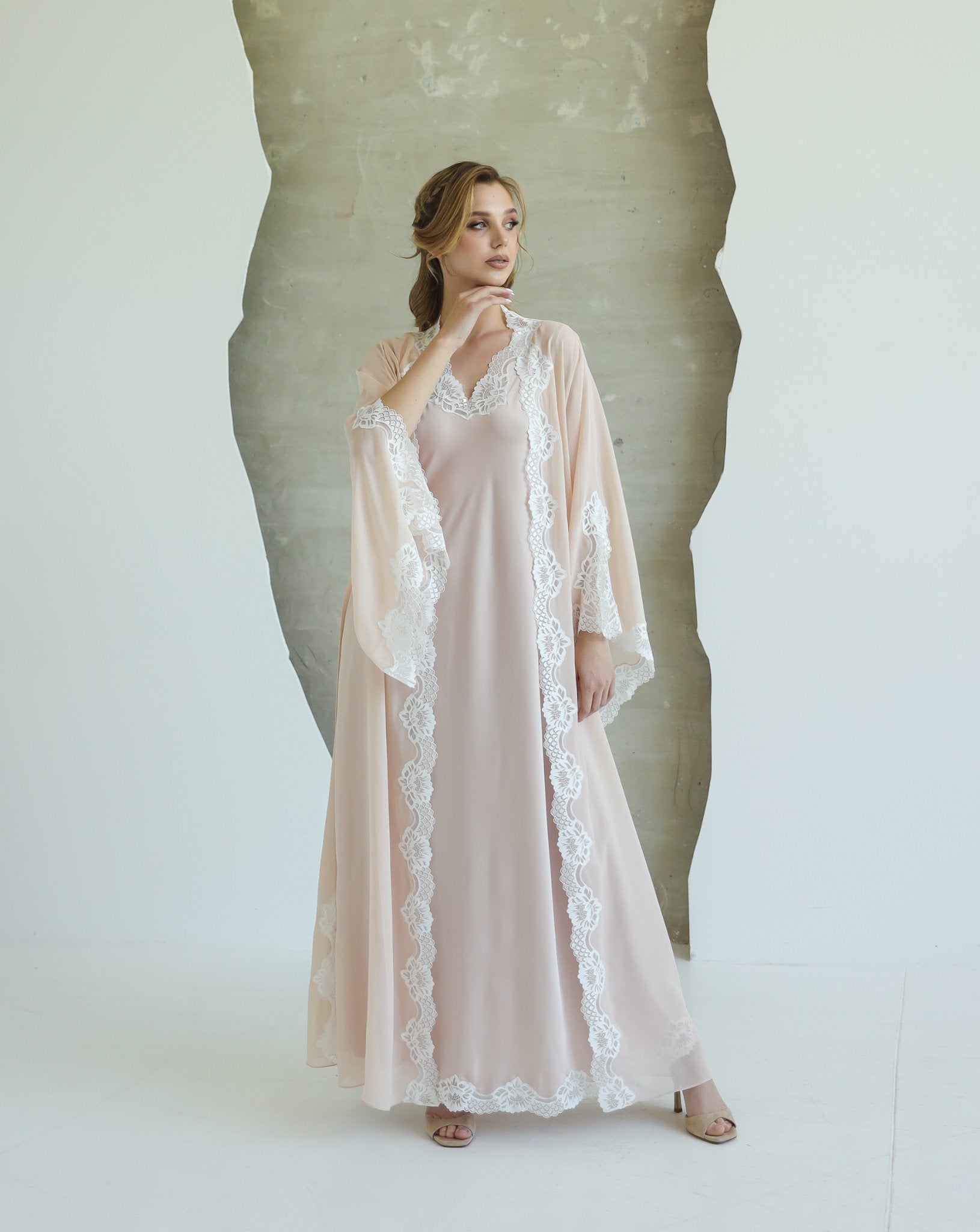 Woman wearing beige robe and nightgown set with lace, standing in front of a light backdrop