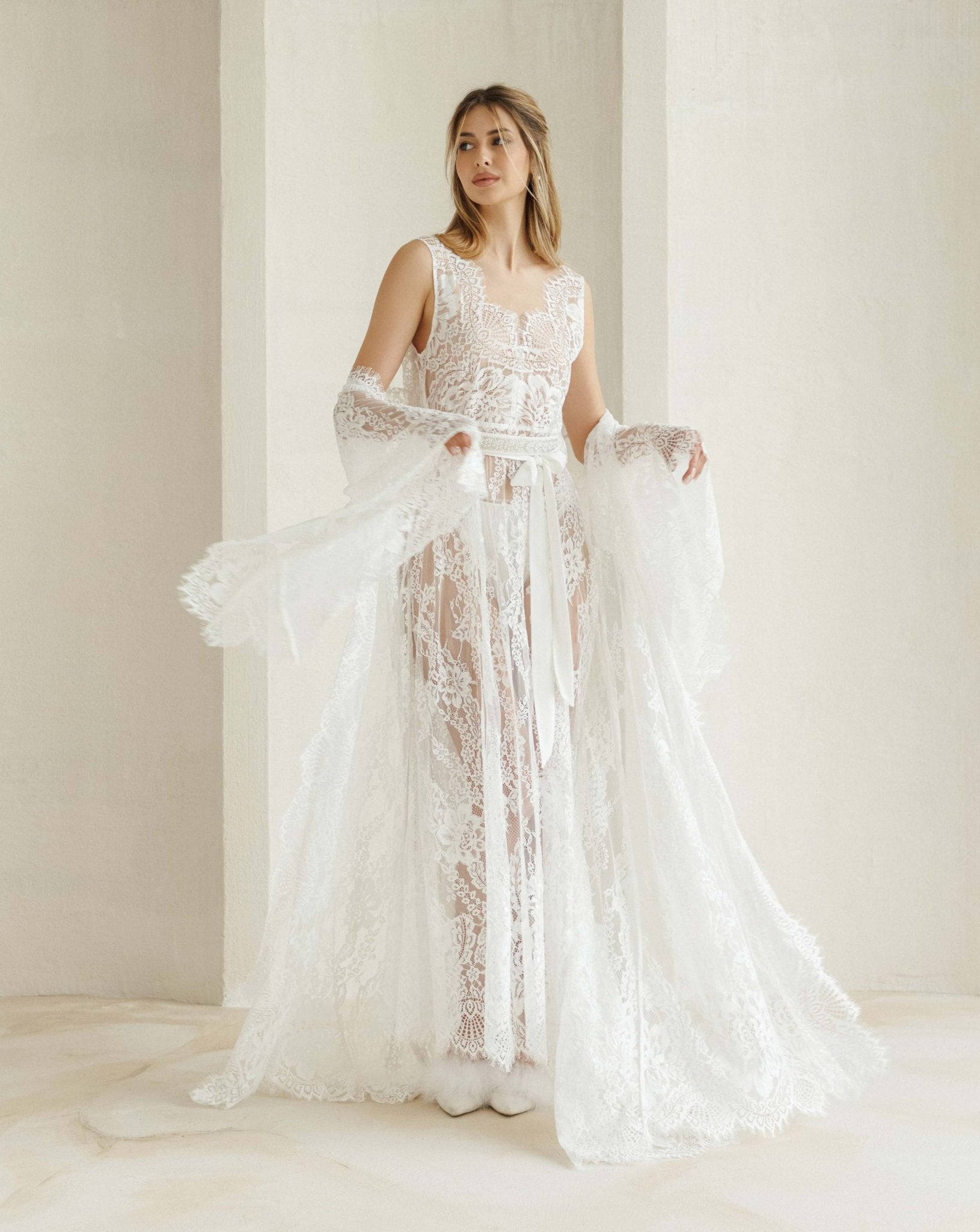 A flowing Bridal Robe draped at the elbows, showcasing the long train and striking lace patterns in motion.