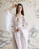 Mid-length shot of a white lace garment with a hand raised, highlighting the wide, airy sleeves and intricate patterns.