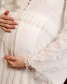 Close-up maternity shot focusing on the lace-embellished sleeves and the delicate ruffle framing the waistline.