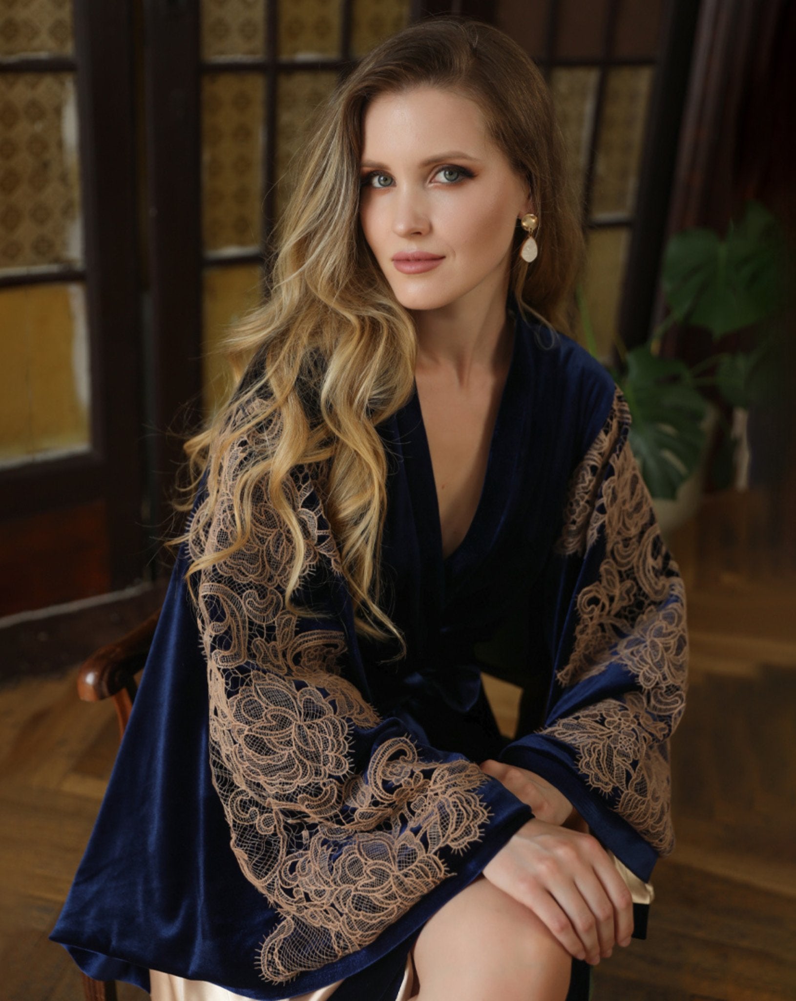 Woman seated in blue velvet robe with gold lace cuffs – luxury loungewear by Kafemme