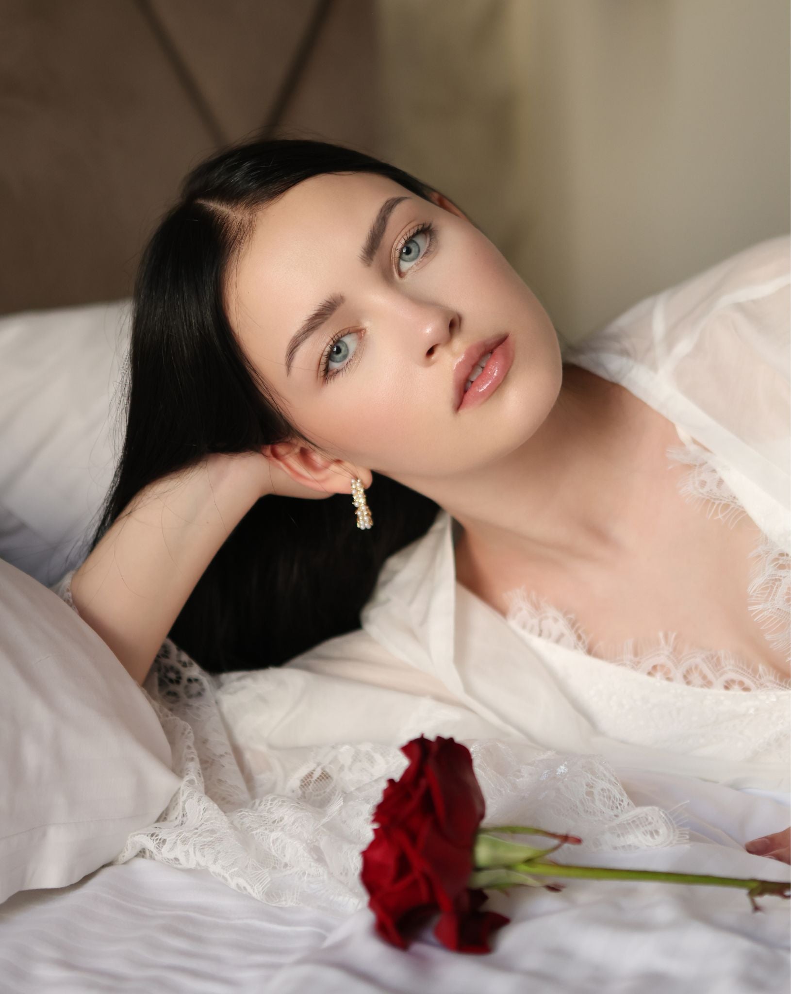 Creative shot of a woman lying on a bed with a red rose, wearing a soft lace-trimmed silk-cotton garment.