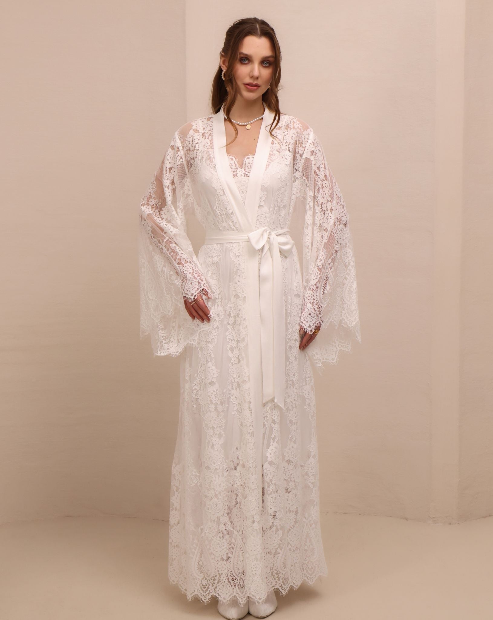 A frontal view with hands on hips, emphasizing the wide lace-finished sleeves and the defined waistline.