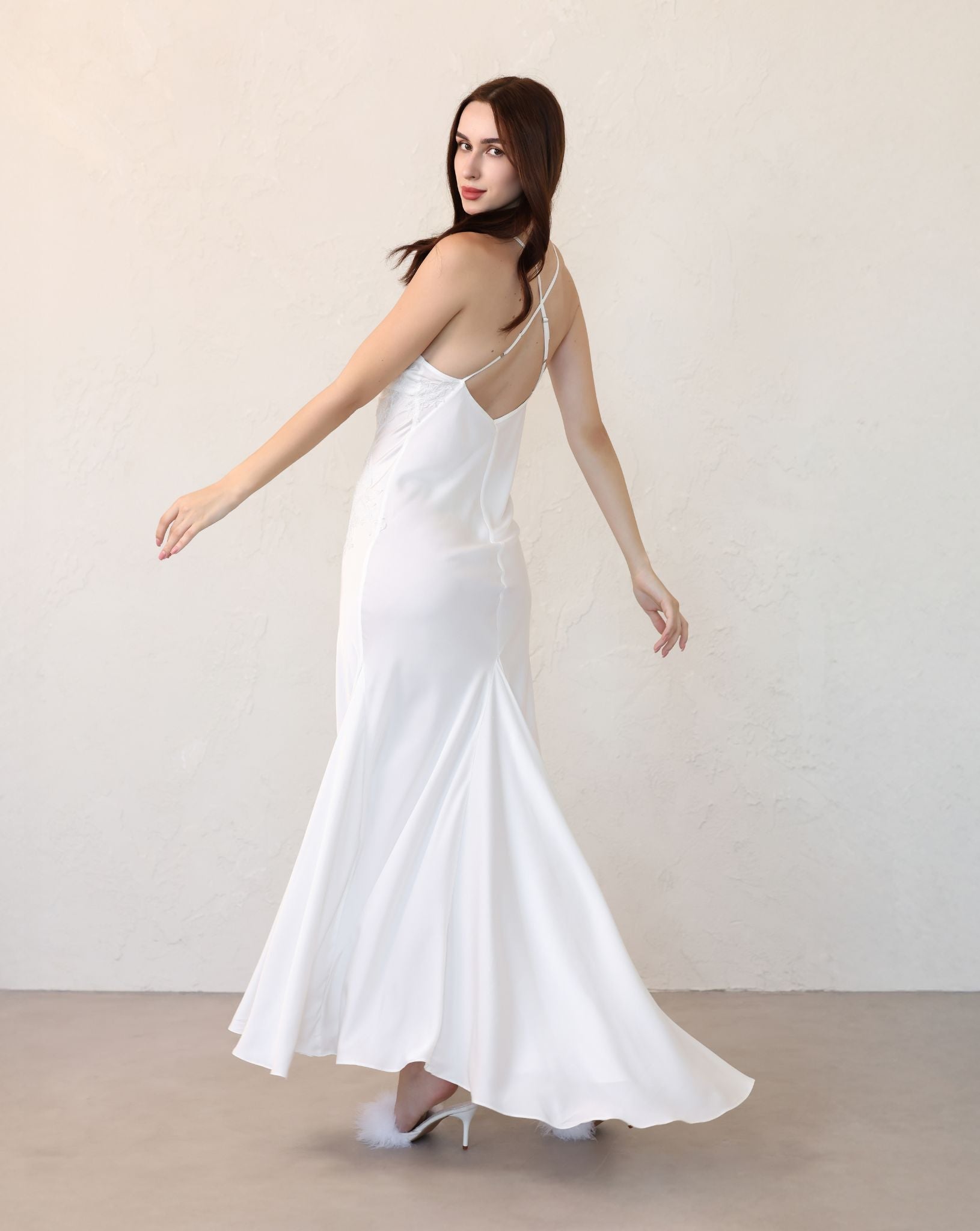 Rear view of a matte liquid satin nightgown in motion, highlighting the seductive strappy back and elegant long train.