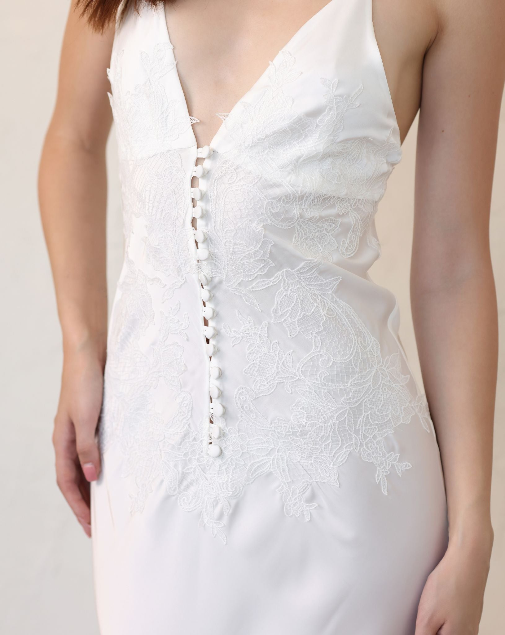 Close-up of a white satin nightdress featuring a seductive decollete and a row of elegant tonal buttons.