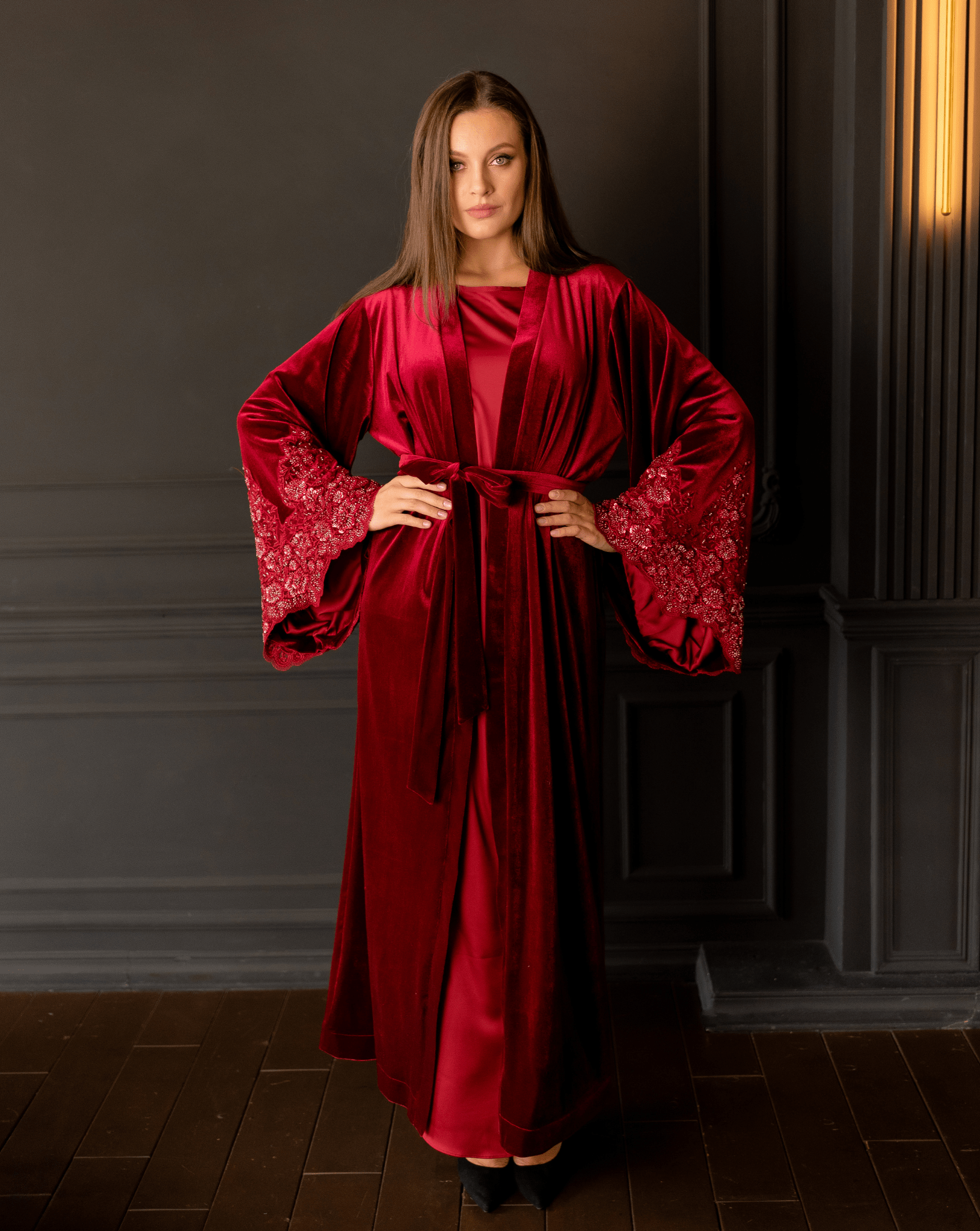 Full-length pose with hands on the hips to highlight the shimmering sleeve embellishments and floor-length hem.