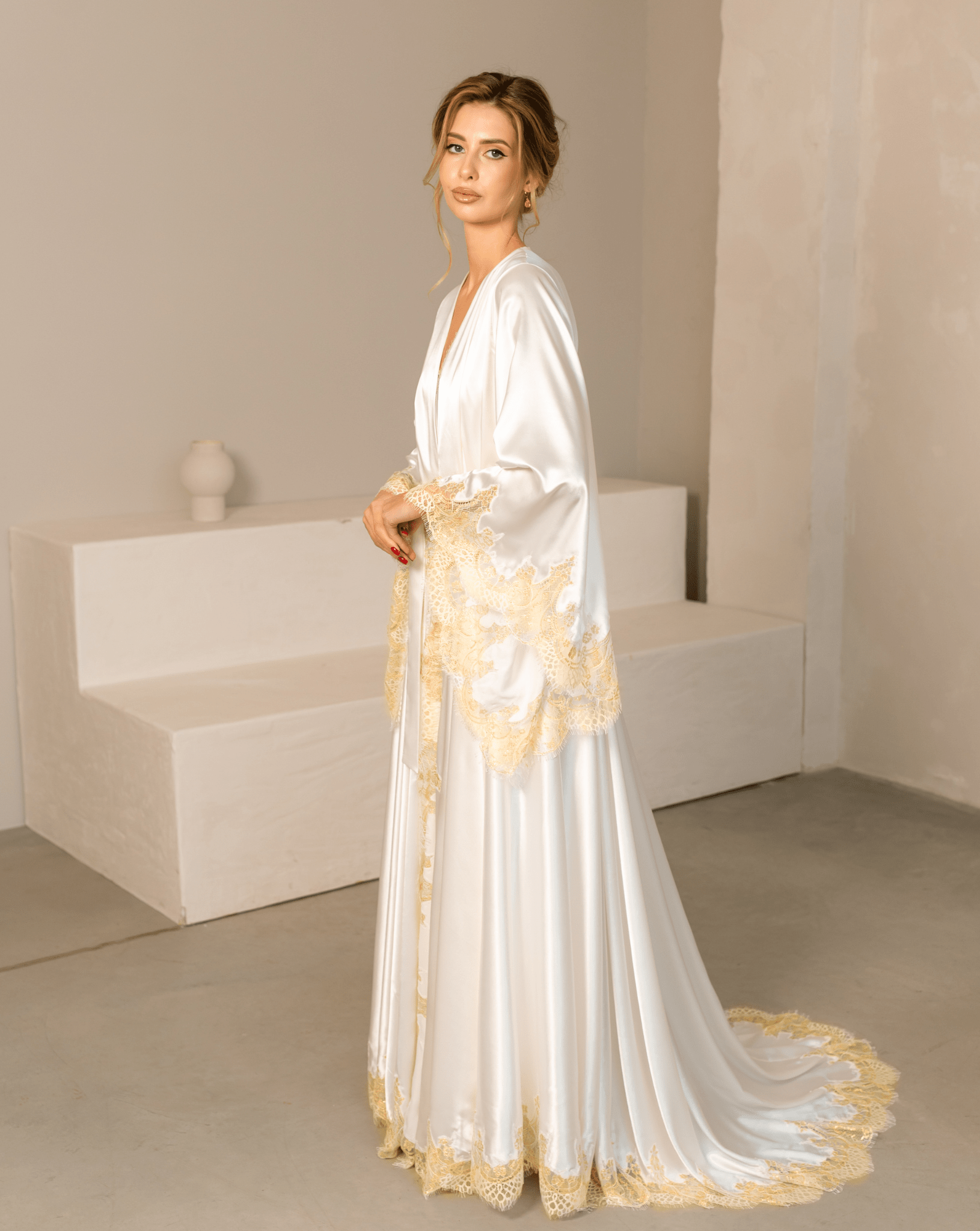 Side view of a white satin robe with a long flowing train and decorative gold lace along the edges.