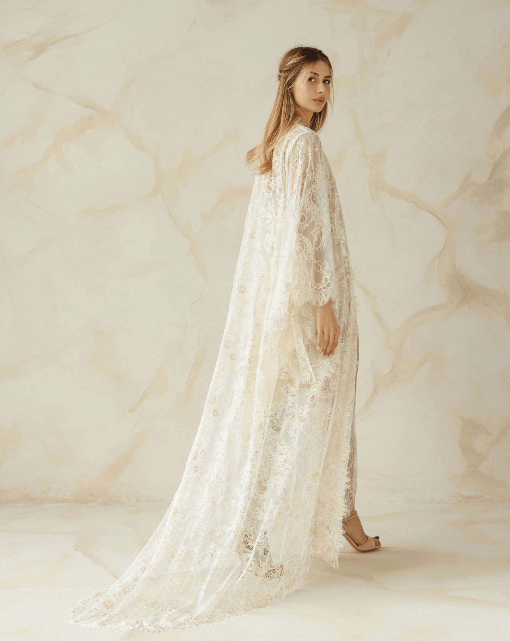 Full-length view of a woman wearing a sheer ivory lace robe over a satin nightgown