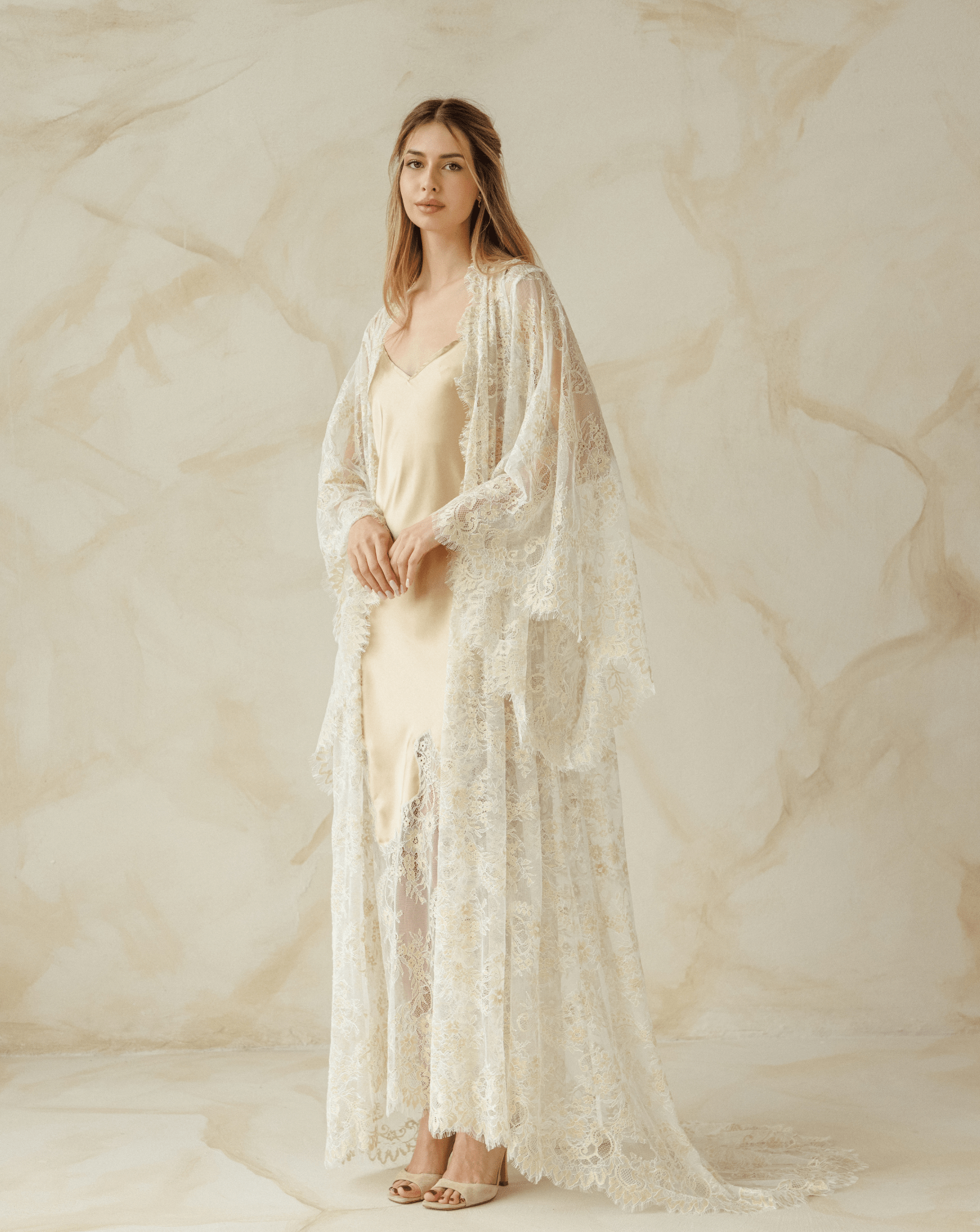 Woman layered in delicate robe over satin gown, hands resting on belly