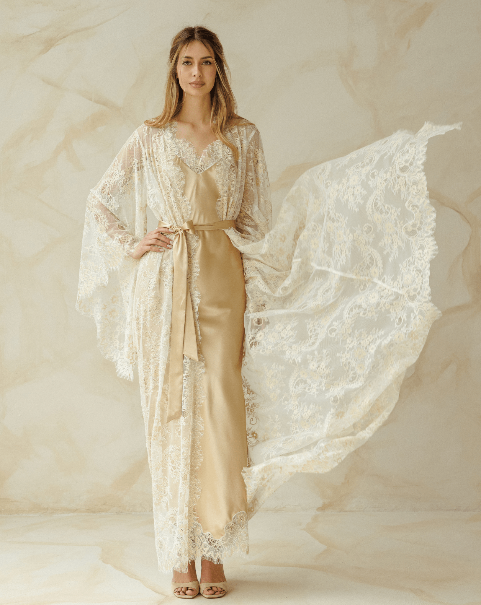 Model posing in an ivory lace robe over a long nightdress, arms slightly lifted